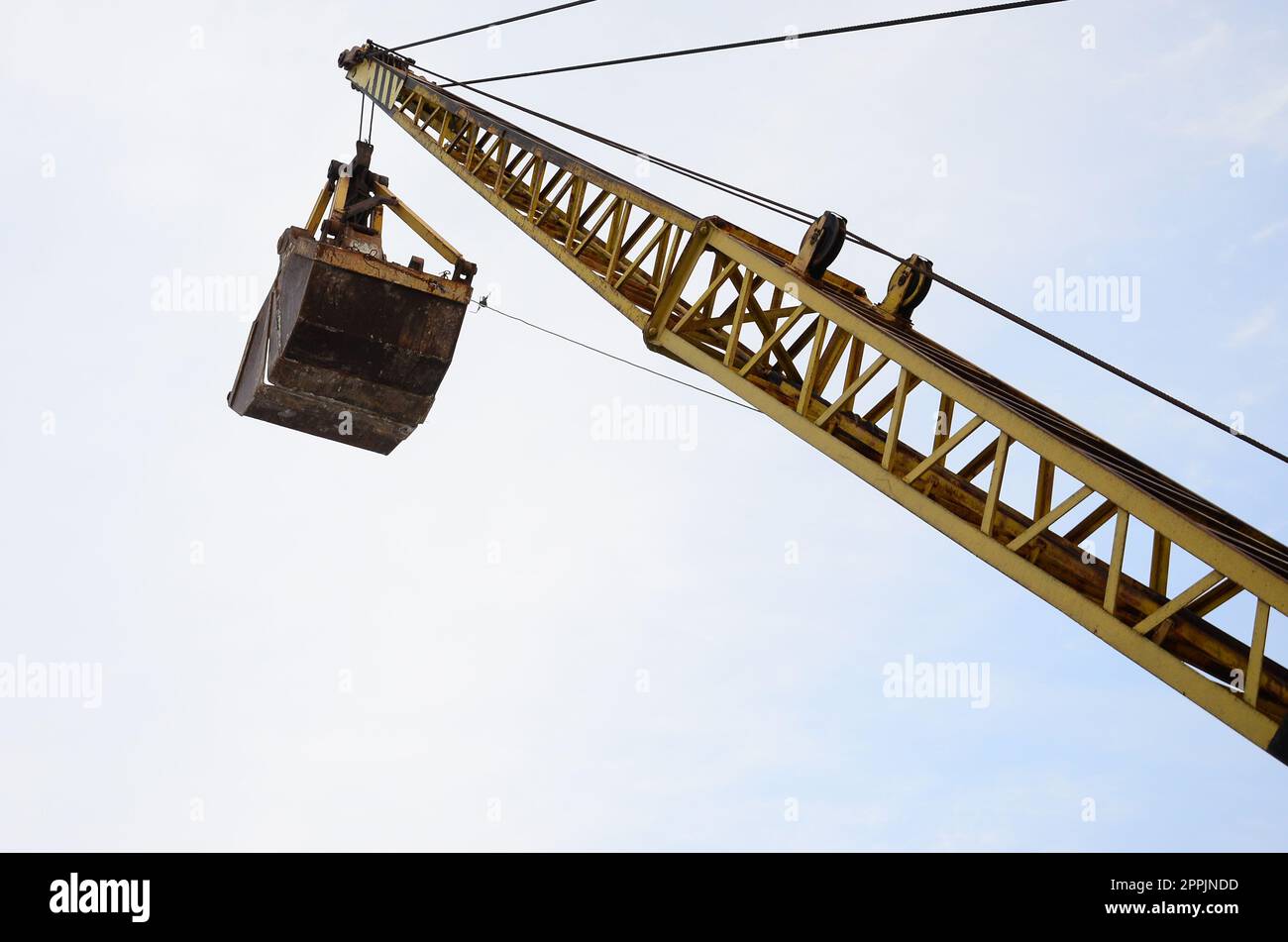Old yellow mechanical clamshell grab on blue sky background Stock Photo