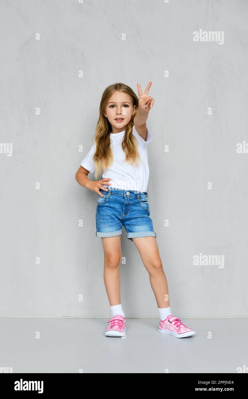 Little girl in tshirt, jeans shorts and sneakers posing near the wall Stock Photo Alamy