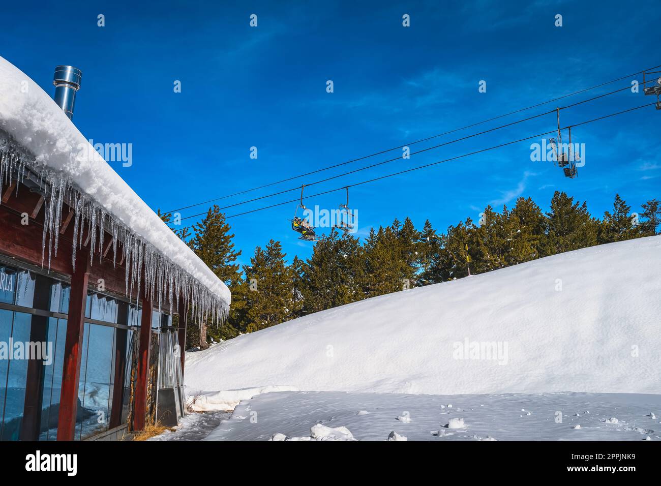 Group of skiers riding up on chair ski lift. Building with icicles hanging from rooftop, Andorra Stock Photo