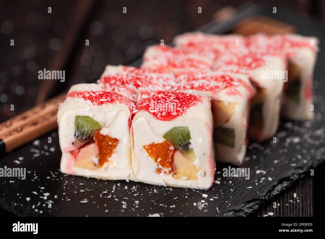 Asian sweet dessert maki sushi close-up - Roll with fruits and cream cheese with coconut flakes and topping Stock Photo