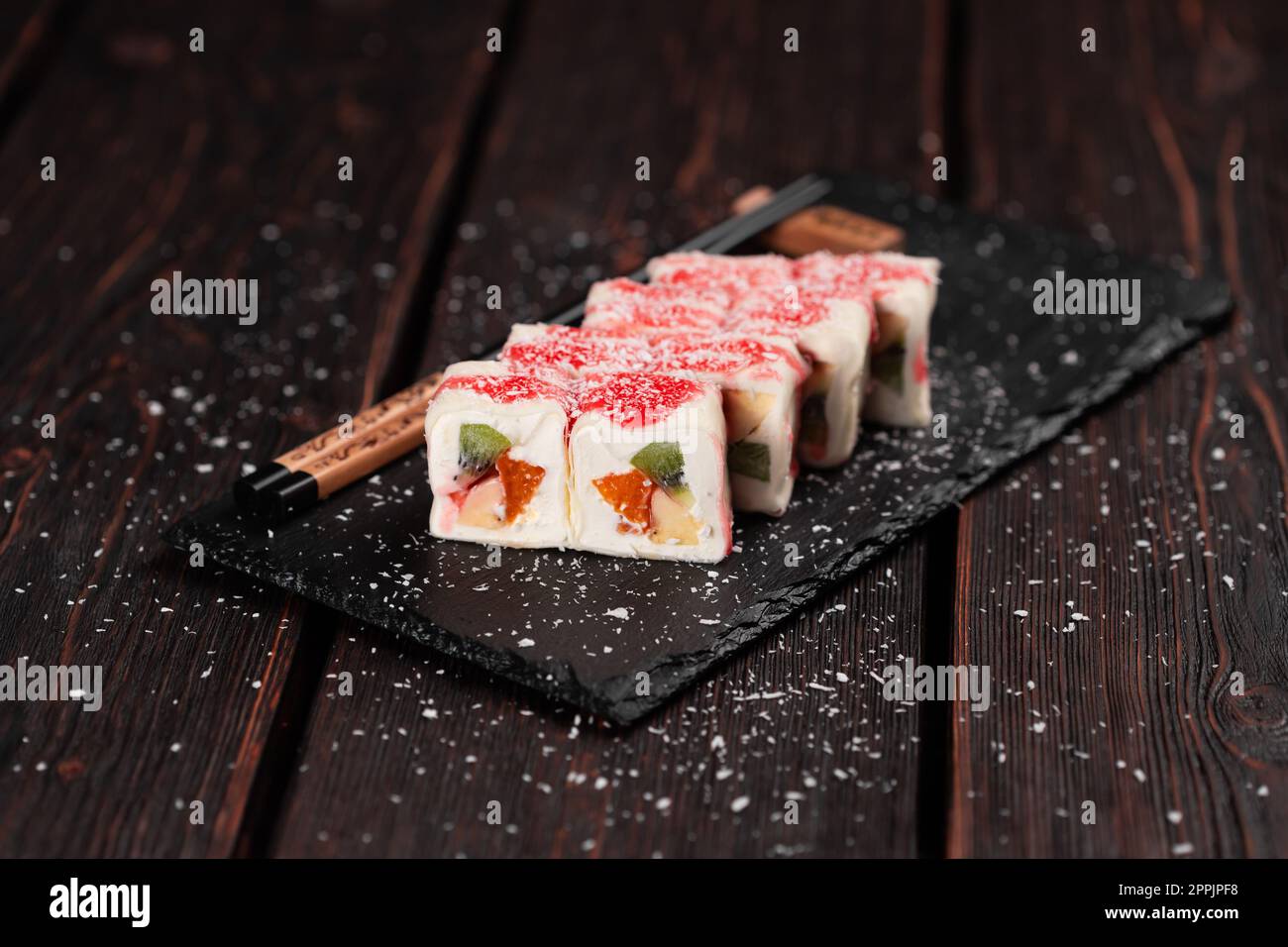 Asian sweet dessert maki sushi - Roll with fruits and cream cheese with coconut flakes and topping Stock Photo