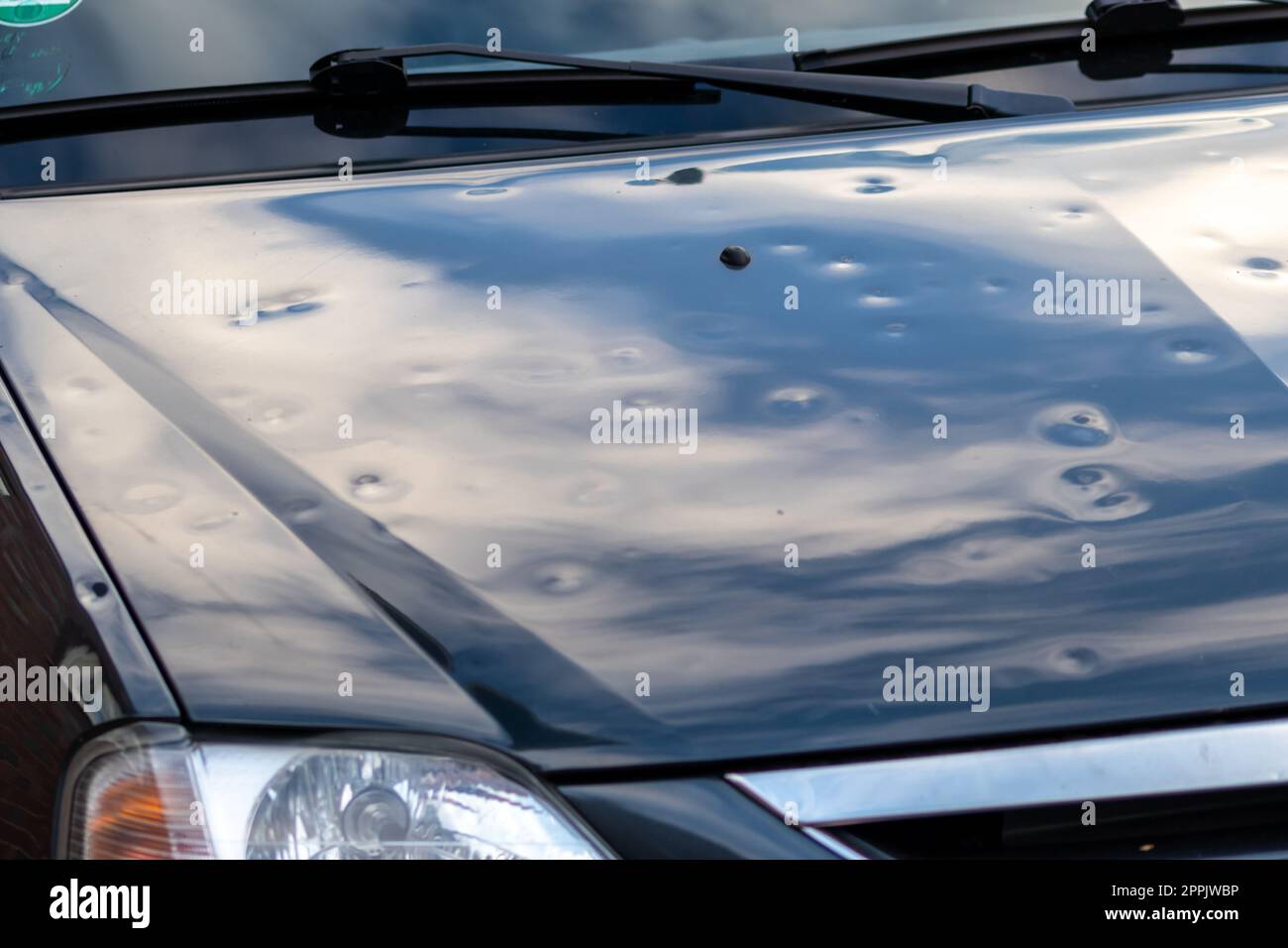 Black car engine hood with many hail damage dents show the forces of