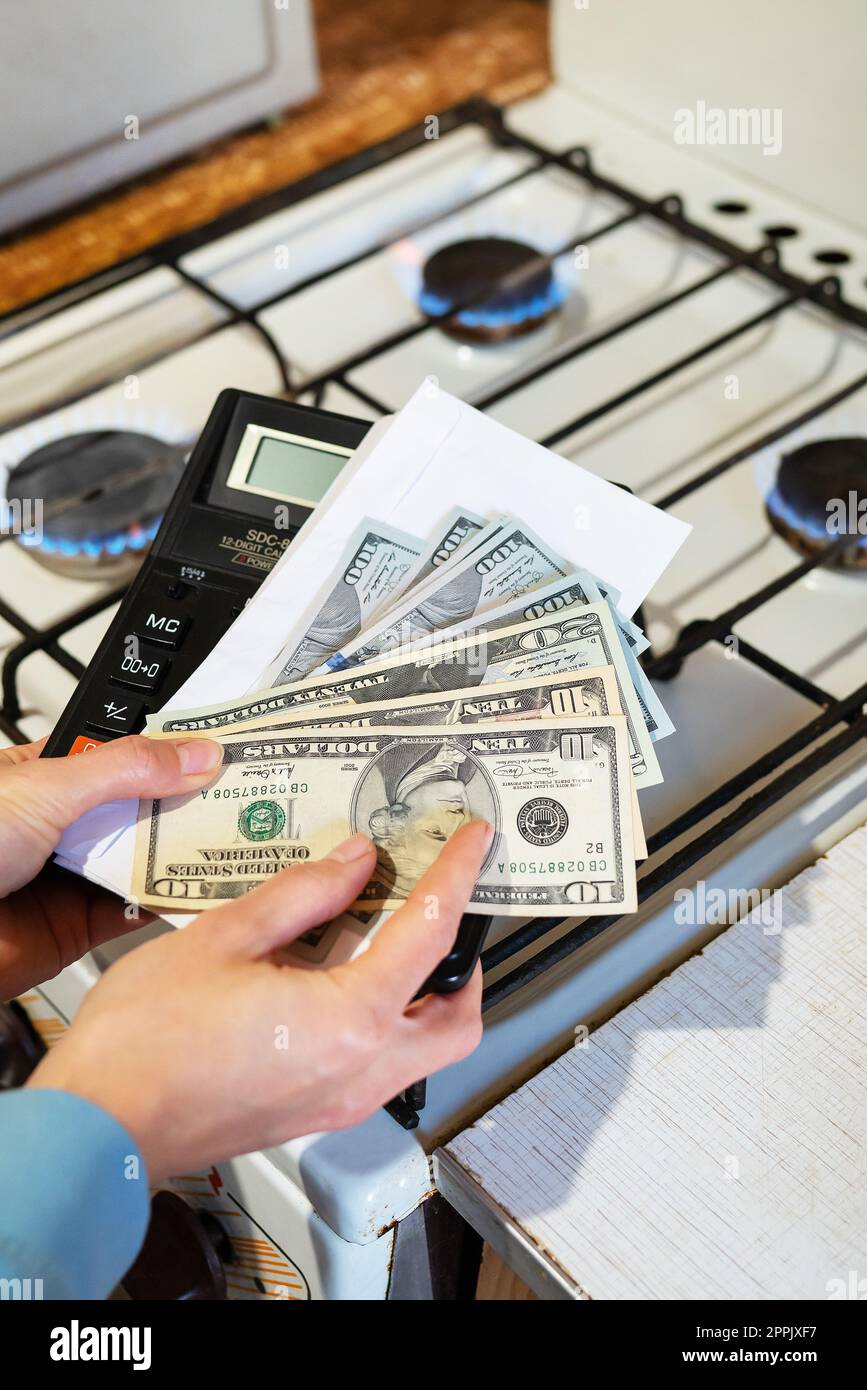 Payment of utility bills, calculations on a calculator. Euro and dollar bills lie near a burning gas burner. The concept of increasing the cost of natural gas supply and payment. Energy crisis, vertical photo. Stock Photo