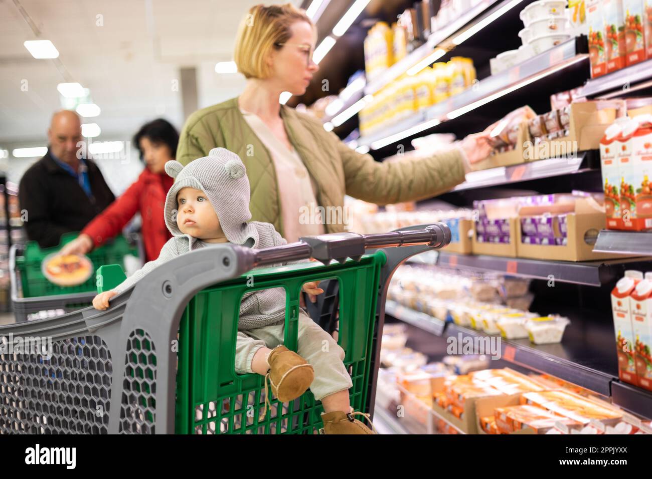 Casualy dressed mother choosing products in department of supermarket ...