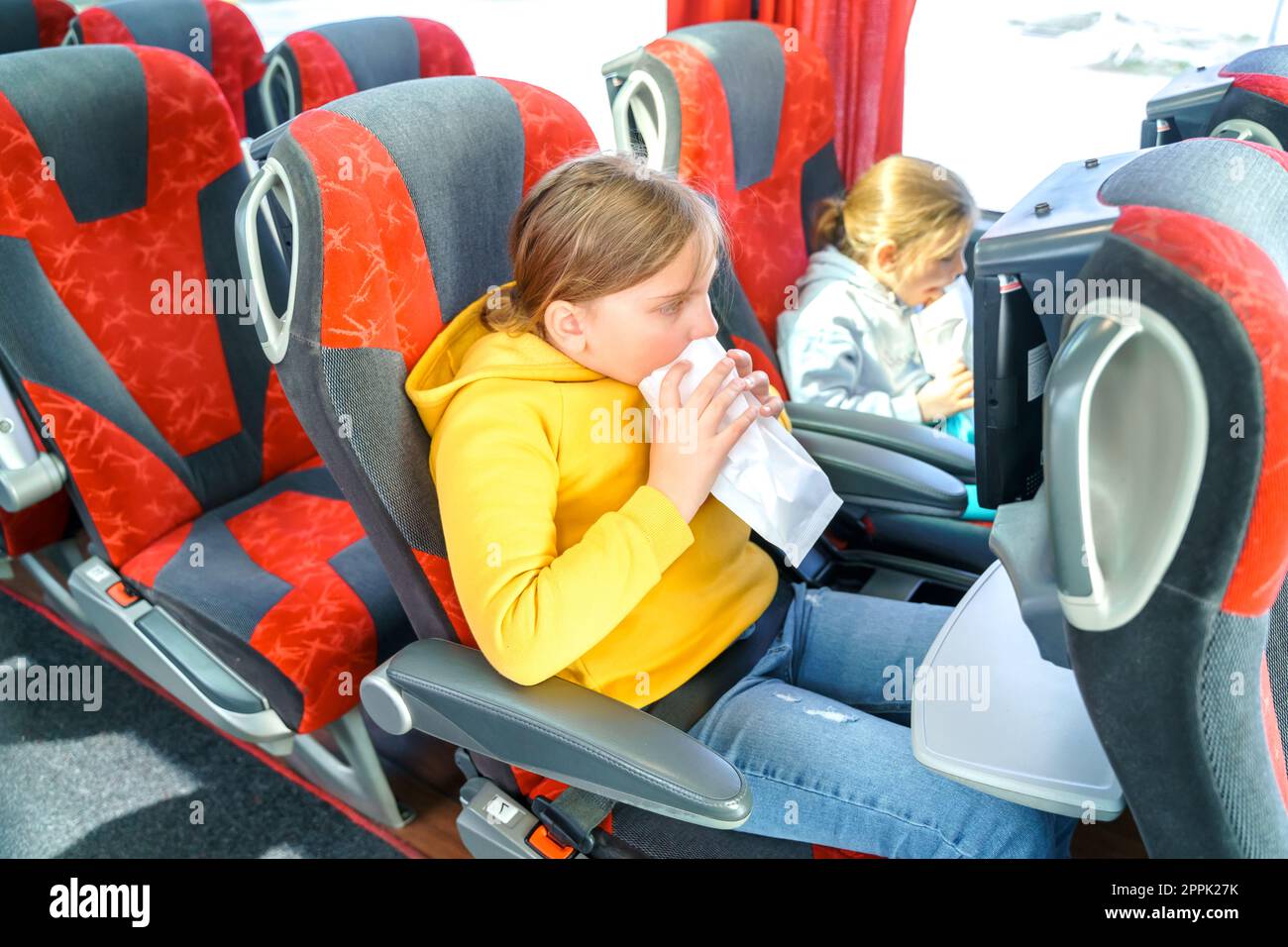 Girl is sick, vomits in bag. Bus road traveling. Girl kid feels bad, rides on large comfortable sightseeing excursion bus. Sitting watching movie cart Stock Photo