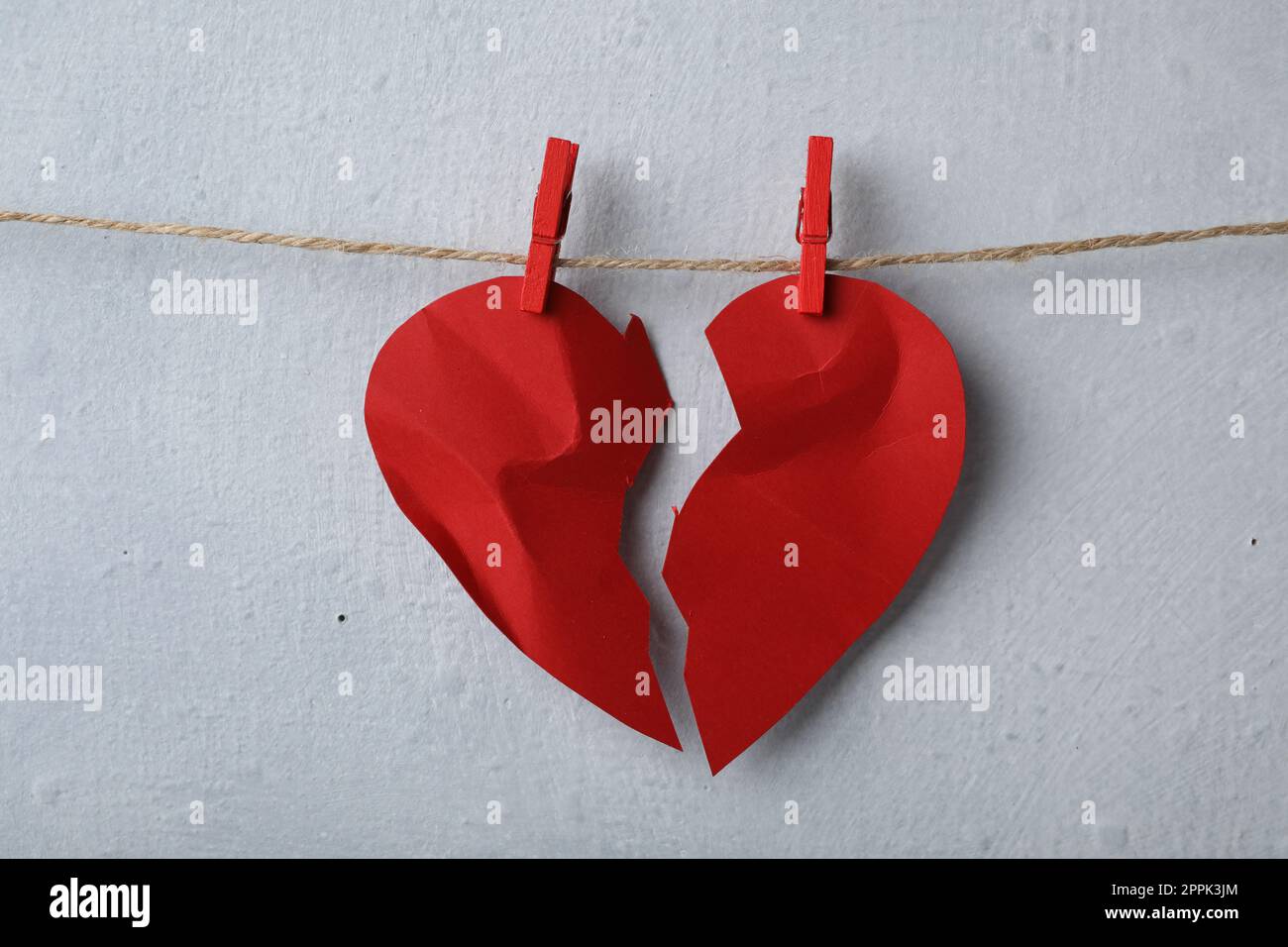 Halves of torn paper heart pinned on laundry string near light wall. Relationship problems concept Stock Photo