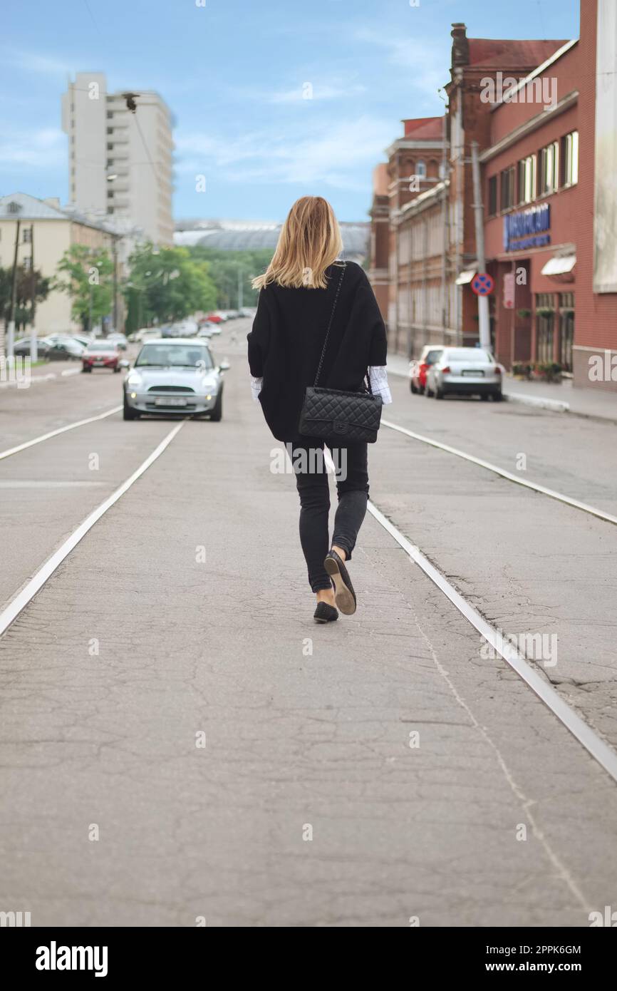 Belarus, Minsk August, 25, 2017 - Hipster girl walking on the centre of the street in black poncho and jeans Stock Photo