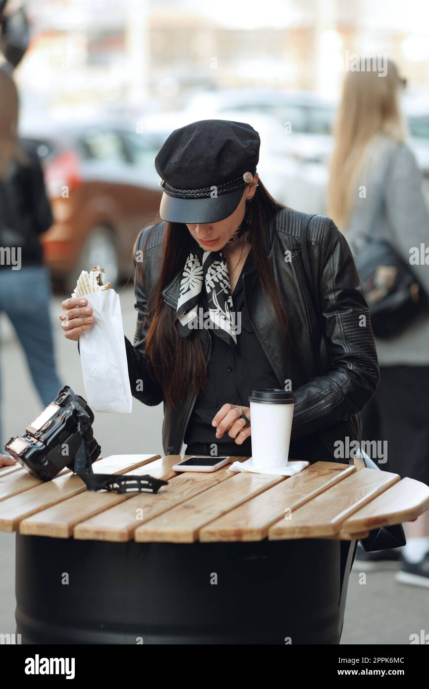Attractive girl eating sandwich on the street cafe and reading news on smartphone Stock Photo