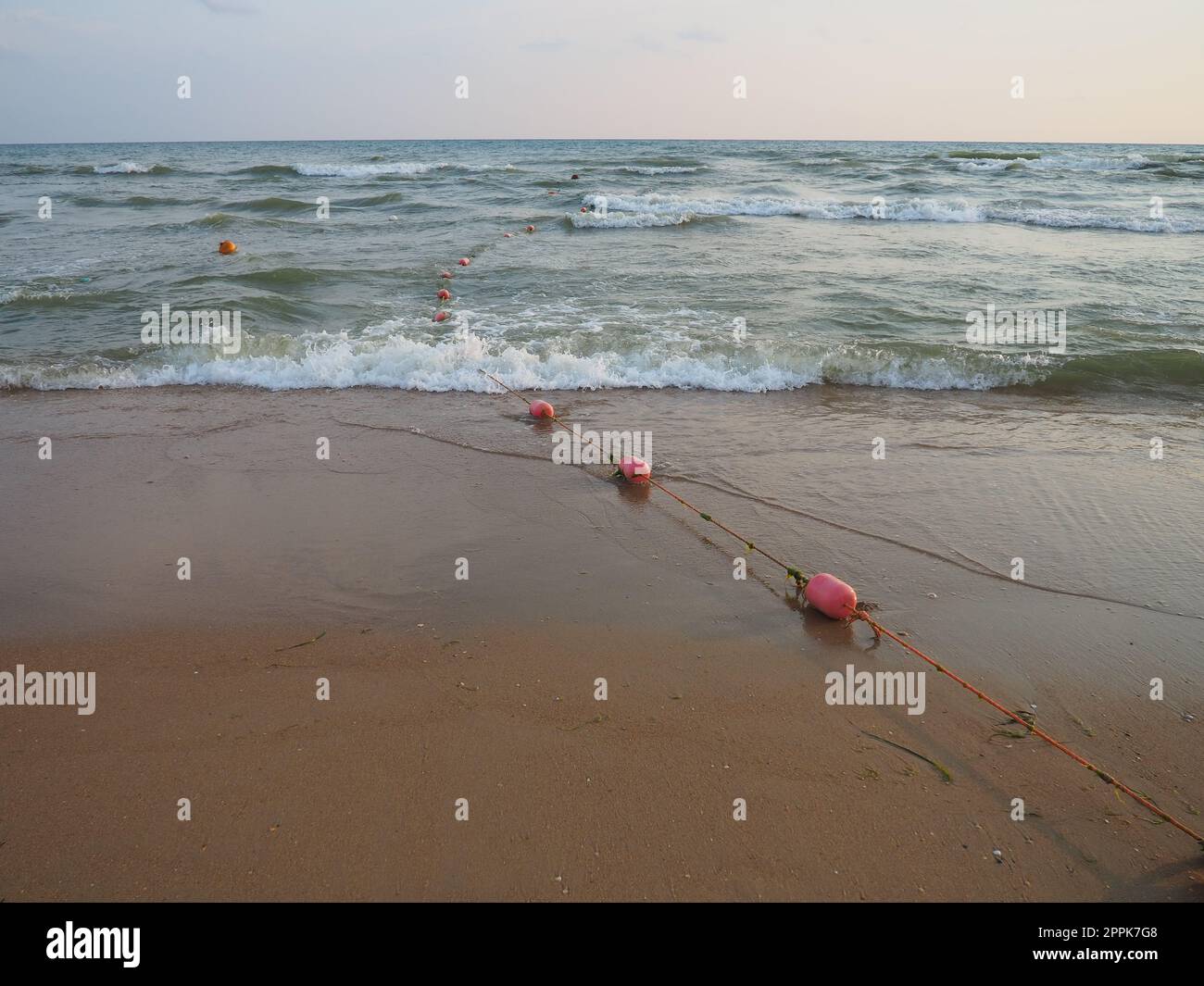 Buoys on a rope near sea water. The buoys are pink restraints to alert people to the depth of the water. Rescue of the drowning. Delimiting a place on a sandy beach between hotels. Wave with bubbles Stock Photo