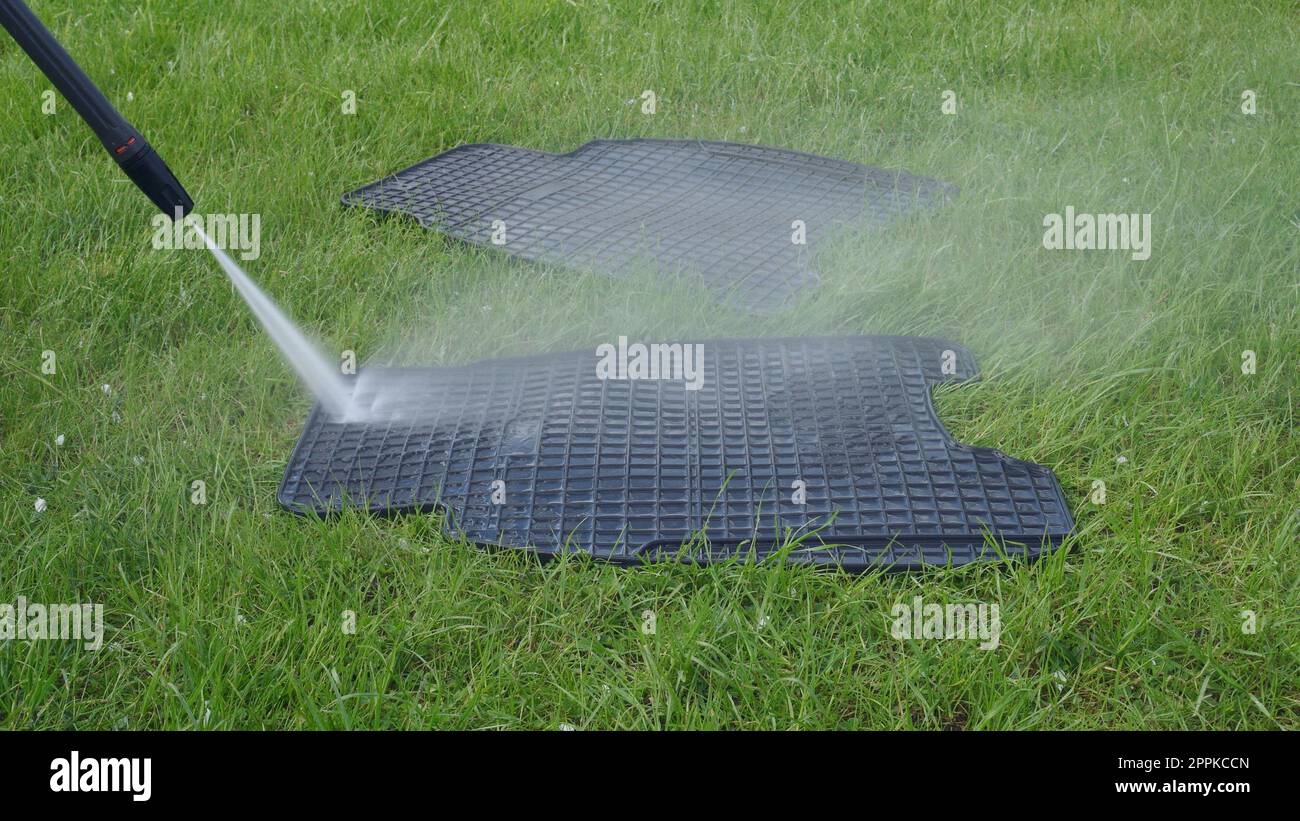 Washing car rubber black mats with manual pressure washer on green lawn. Splashing water clean mat on grass Stock Photo