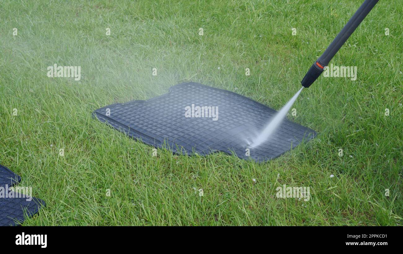 Washing car rubber black mats with manual pressure washer on green lawn. Splashing water clean mat on grass Stock Photo