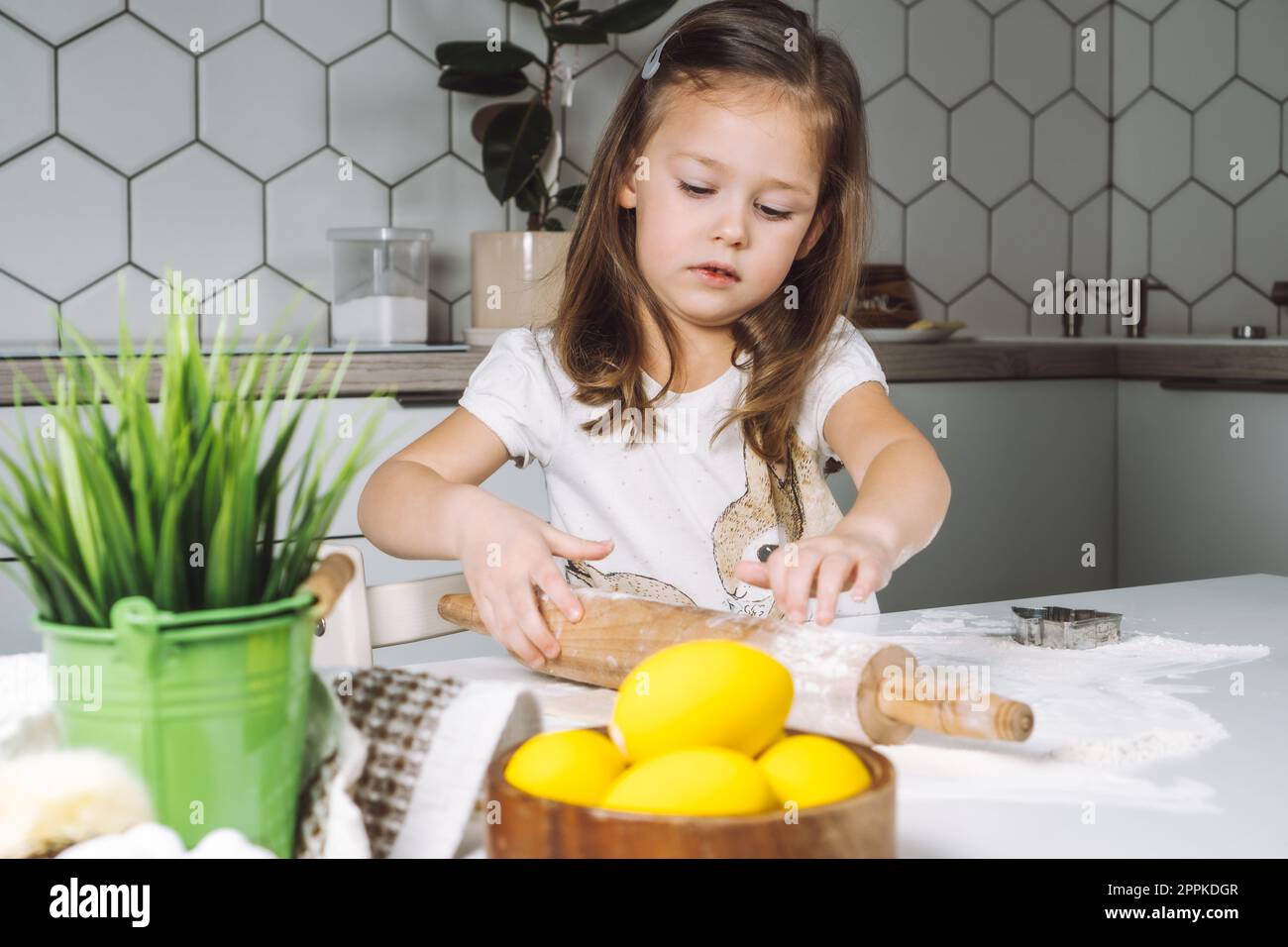 Portrait little serious girl, helping, learning rolling dough, making shape easter cookies. Holding rolling pin. Closeup Stock Photo