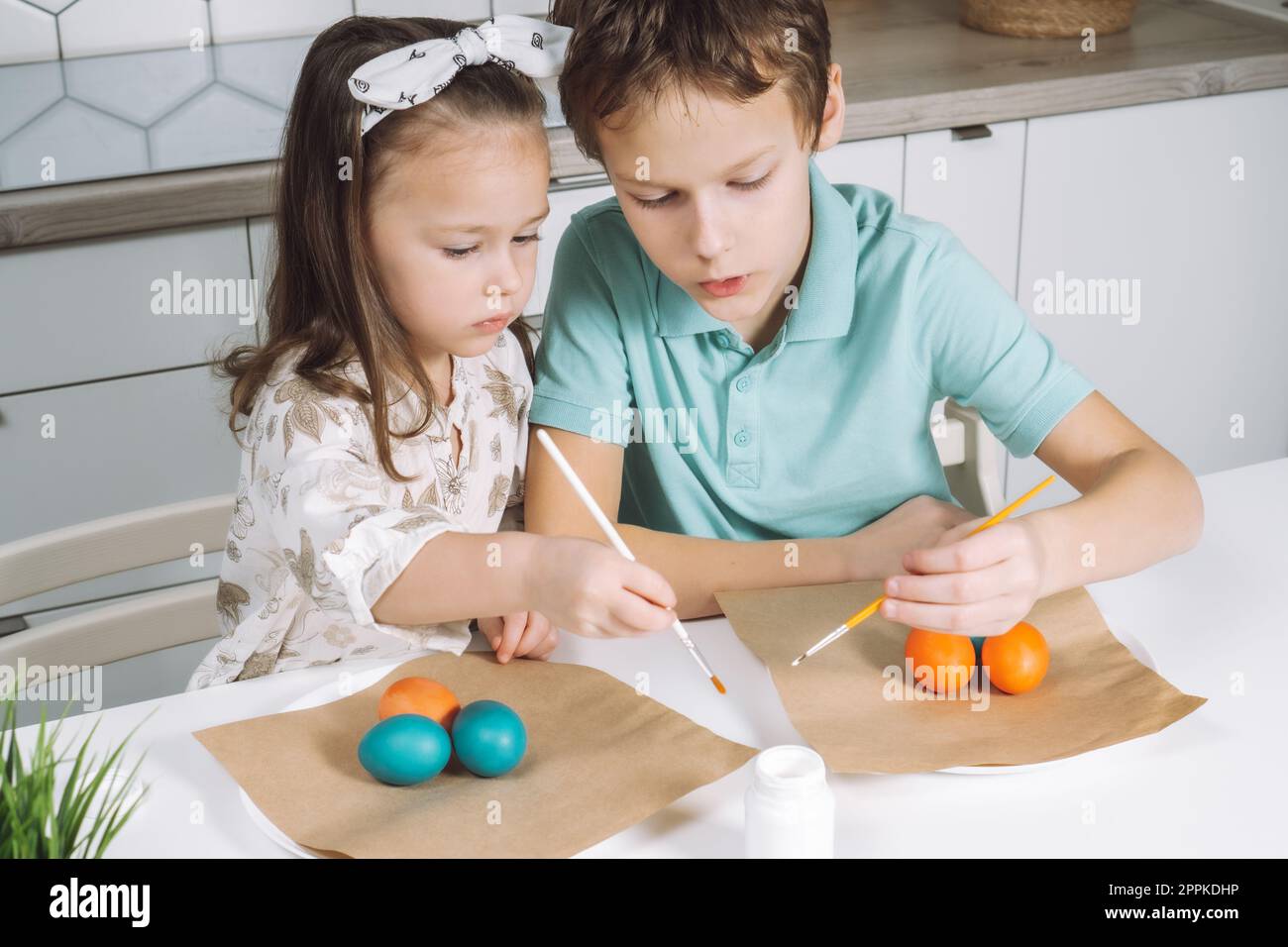 Portrait of enthusiastic joyful two little kids boy and girl, painting brush color Easter eggs. Family holiday tradion Stock Photo