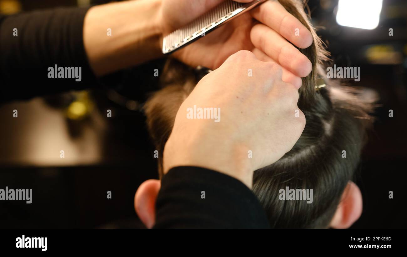 Closeup View Of barber using hair clip to fix the hair for cut and styling it. Hairdresser use pinsn hair salon. service in a modern barbershop in a dark key lightning with warm light back view Stock Photo