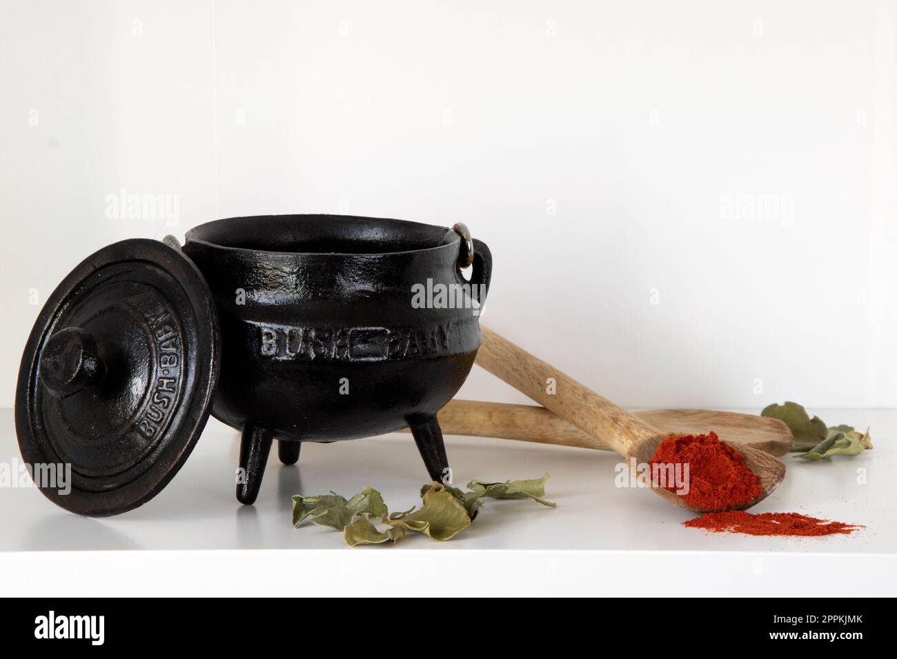 White shelf with three-legged black pot, wooden spoons and paprika Stock Photo