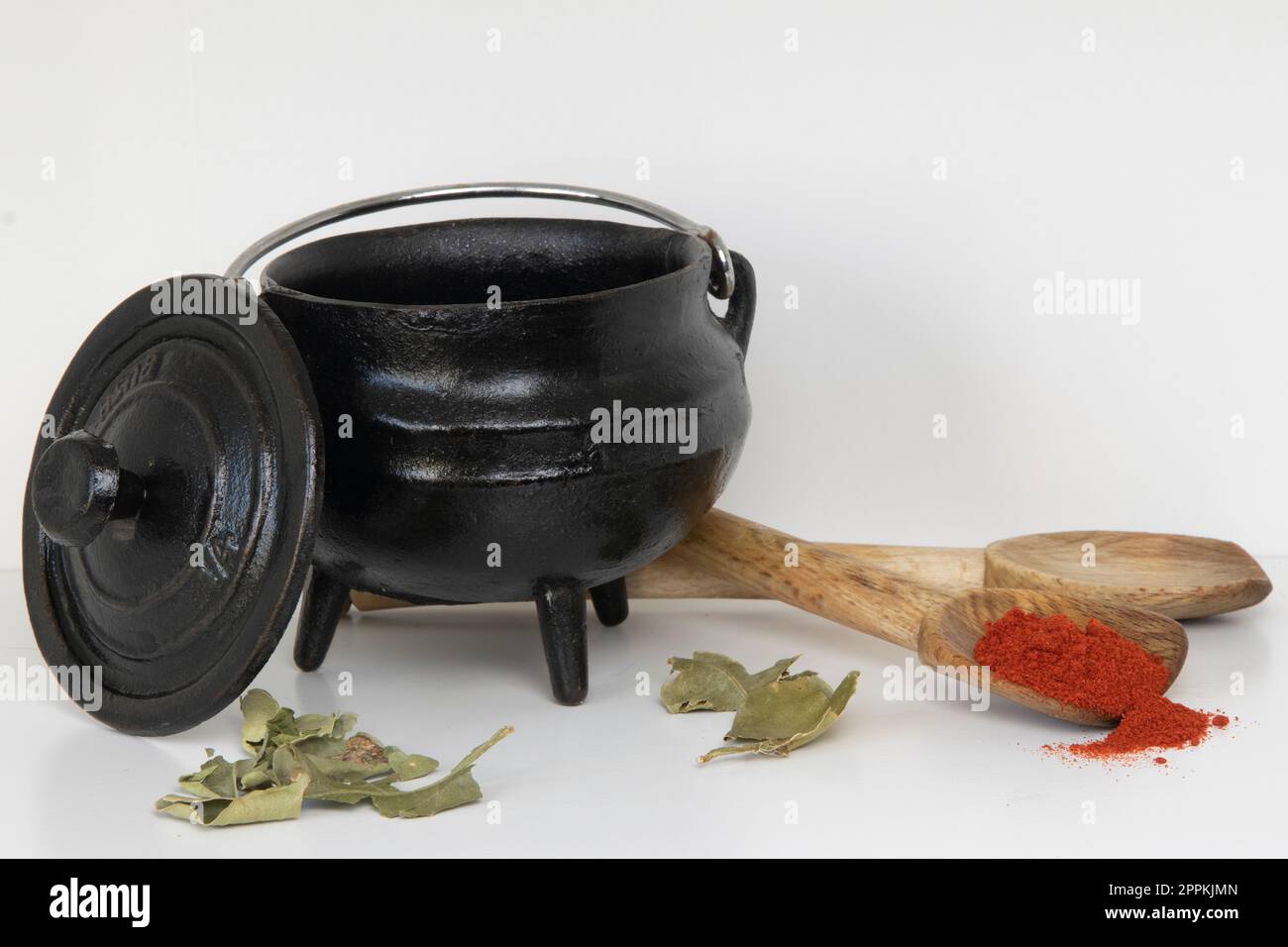 Black threelegged cast iron pot with wooden spoons, paprika, mustard