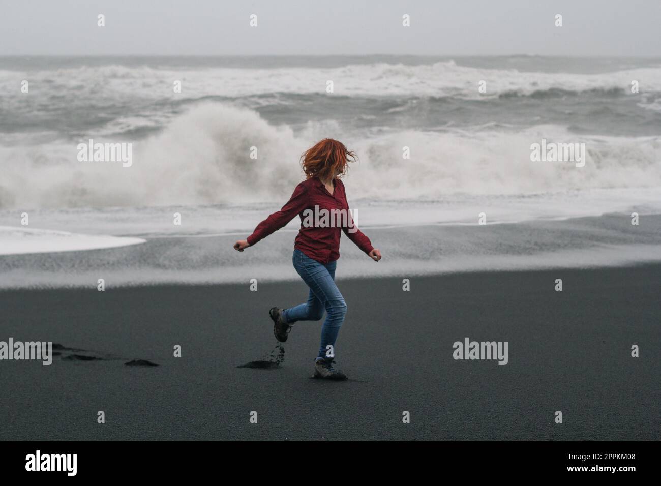 Redhead lady running along black beach scenic photography Stock Photo