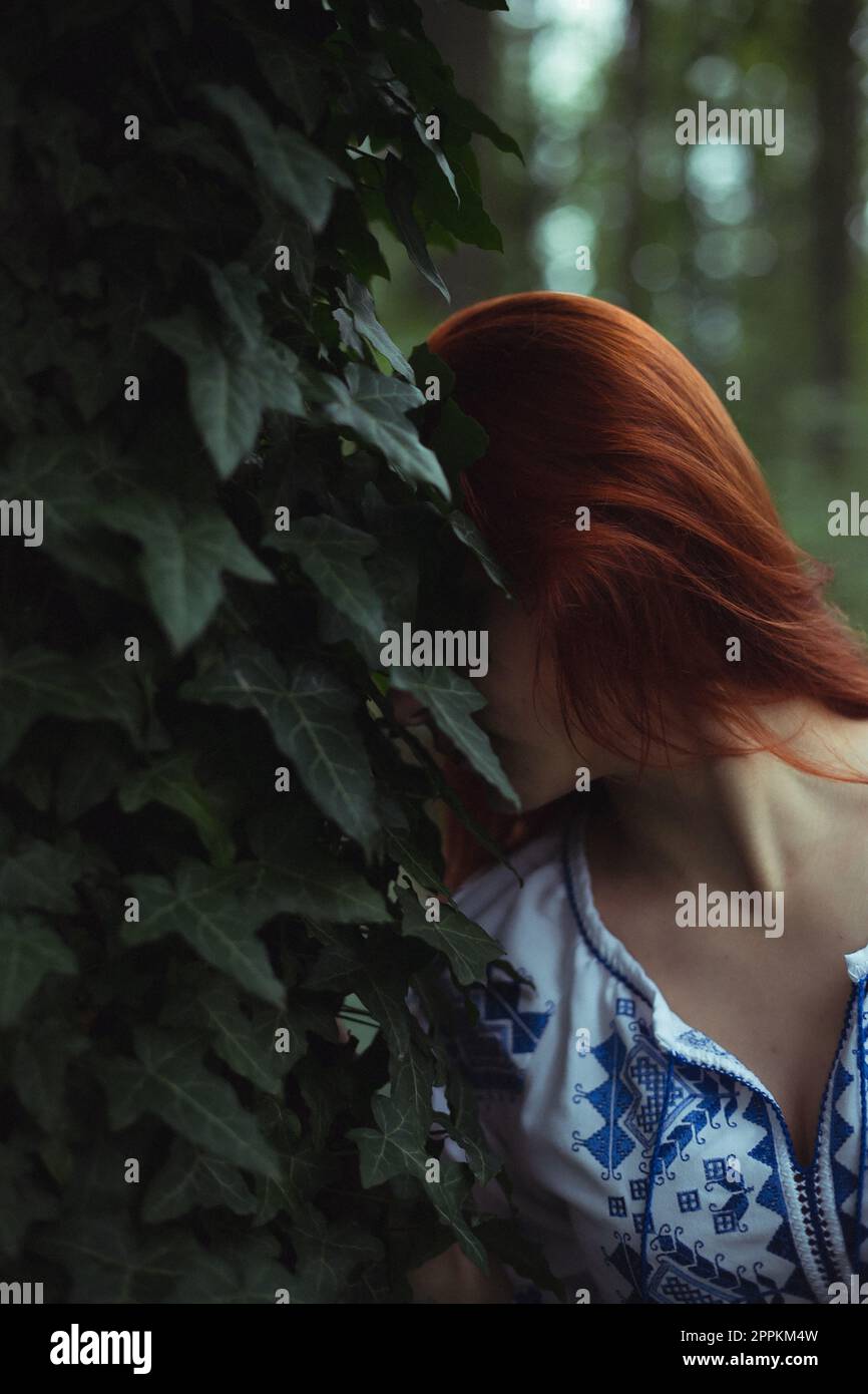 Close up ginger haired woman pressing head against ivy leaves concept photo Stock Photo