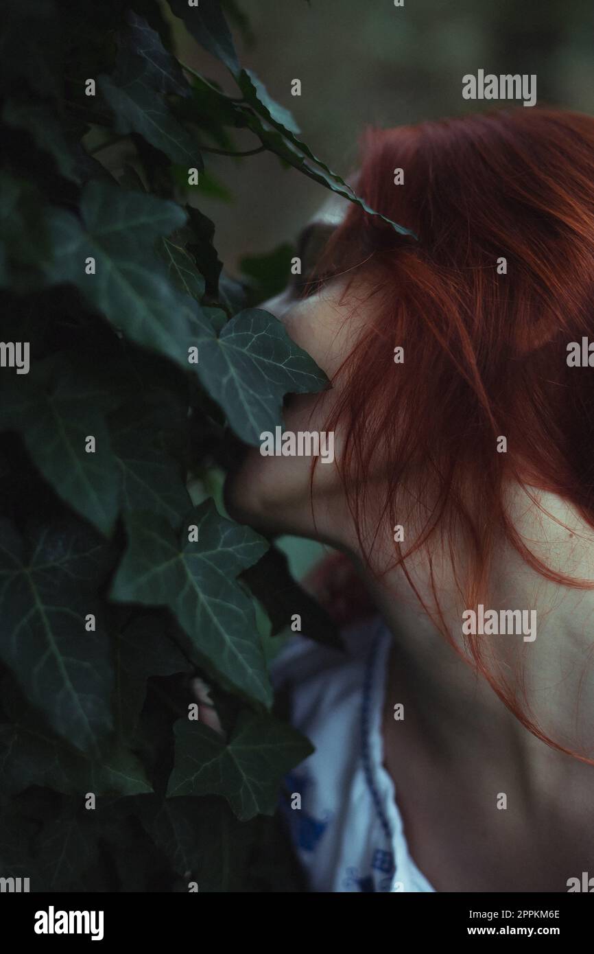 Close up woman with closed eyes hiding face in ivy leaves concept photo Stock Photo