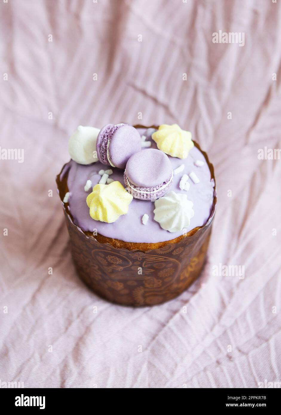 A traditional paska decorated with white Swiss chocolate and meringue stands on a lavender tablecloth. Easter holiday. Stock Photo
