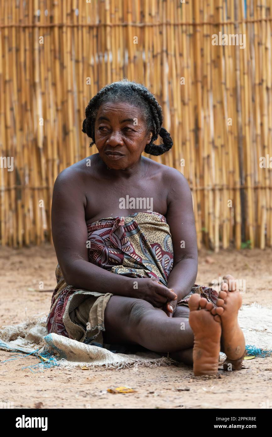 Elder Malagasy woman relaxing in front of hut, there is no job opportunity here. Everyday life on the Madagascar countryside. Stock Photo