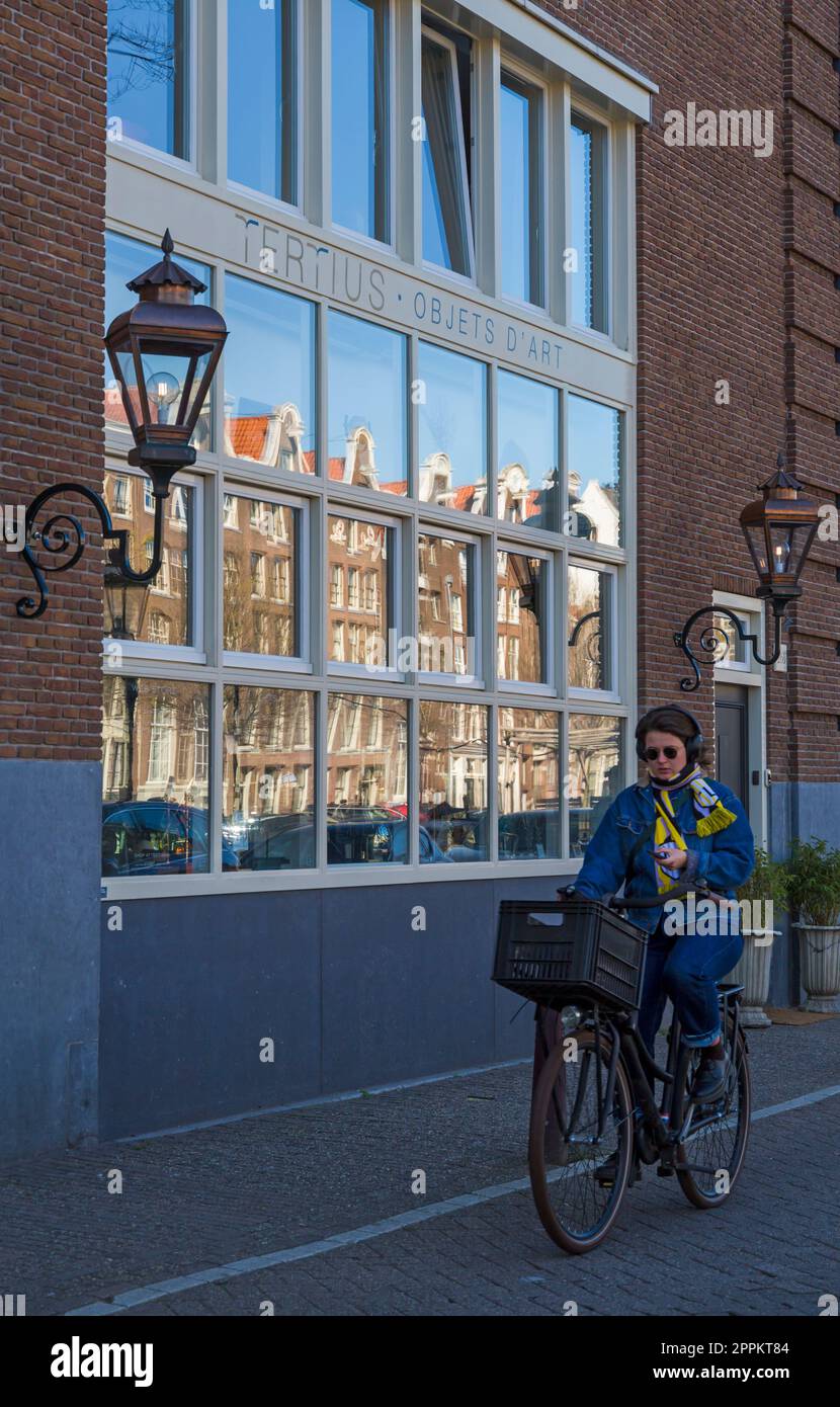 Cyclist cycling past Tertius objets d'art building at Amsterdam, Holland, Netherlands in April Stock Photo