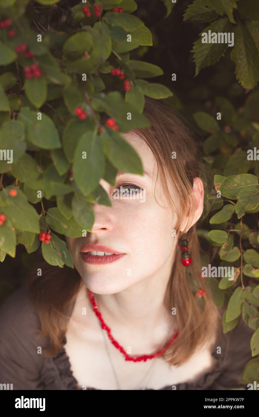 Close up woman peeking through winterberry leaves portrait picture Stock Photo