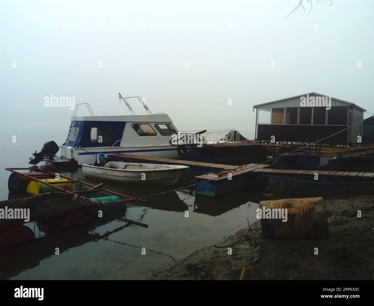 Belgrade, Serbia, January 14, 2020 White boat at the pier, left for the winter. Foggy weather on a January cloudy day. Reflection in the river river. House for shelter from the weather Stock Photo