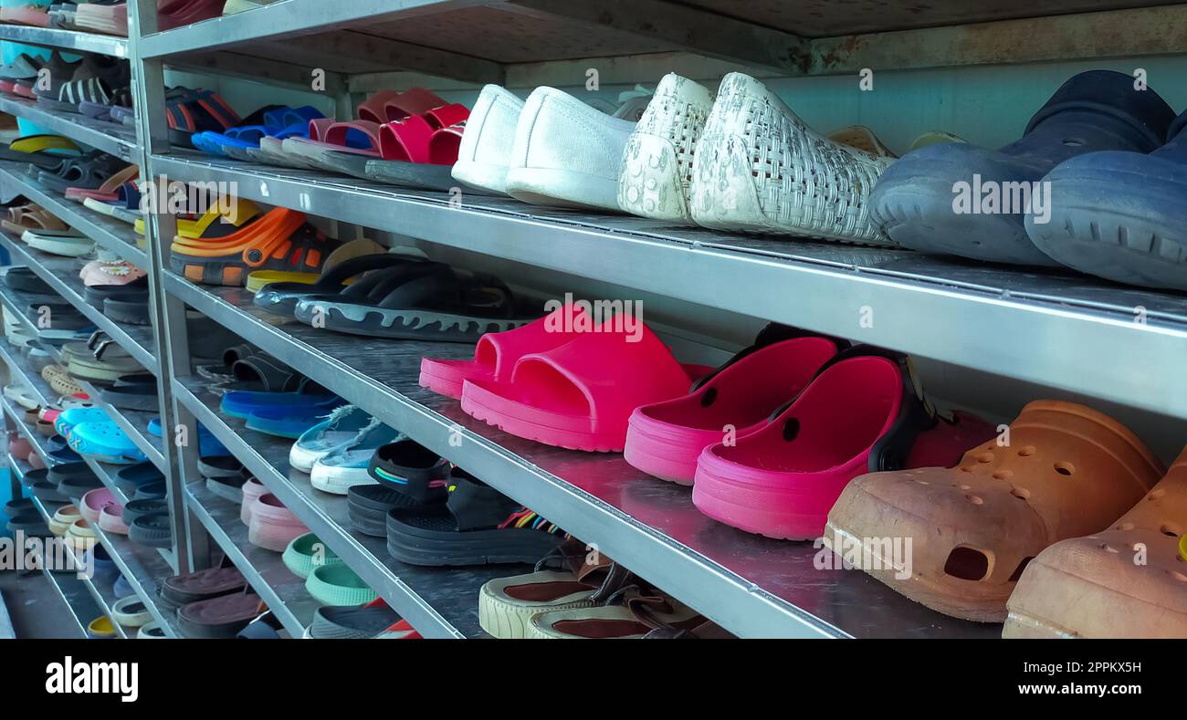 Shoes of workers and visitors in the shoe rack of the factory. Many shoes for men and women are organized on the shoe rack. Footwear in factory concept. Many kinds of shoes, sneakers, and sandals. Stock Photo