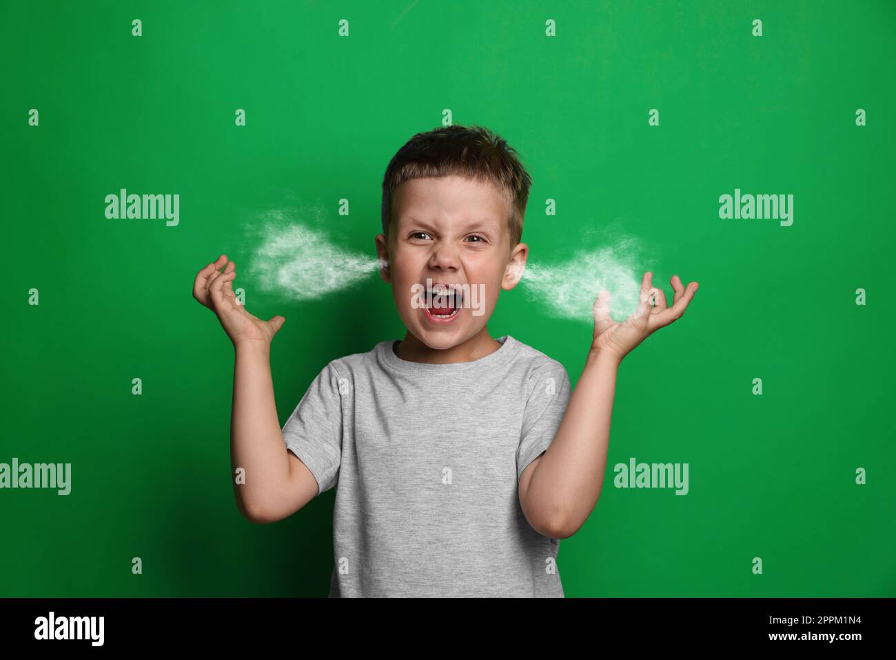 Aggressive little boy with steam coming out of his ears on green background Stock Photo