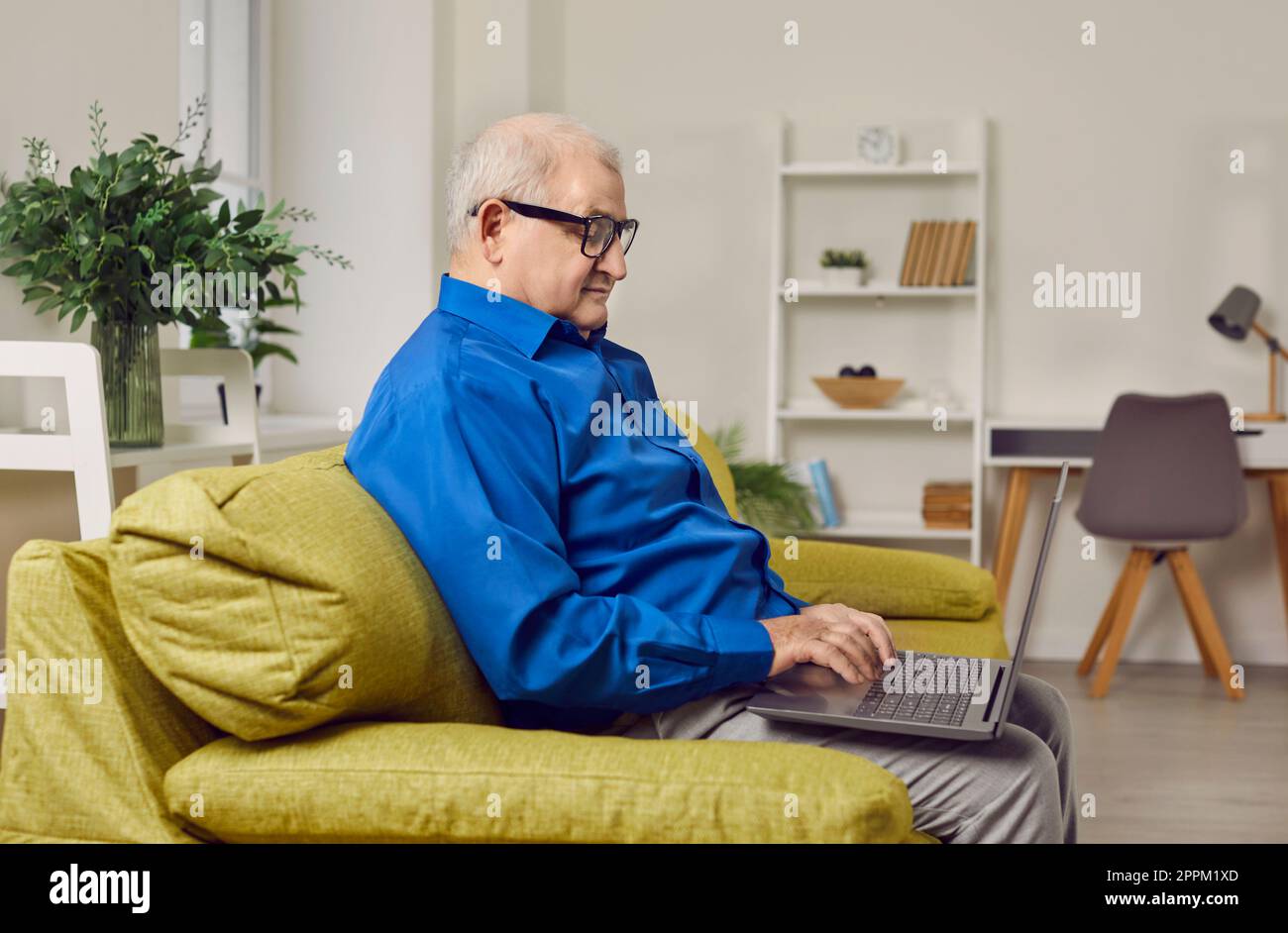 Focused elderly man sitting on sofa using laptop Stock Photo
