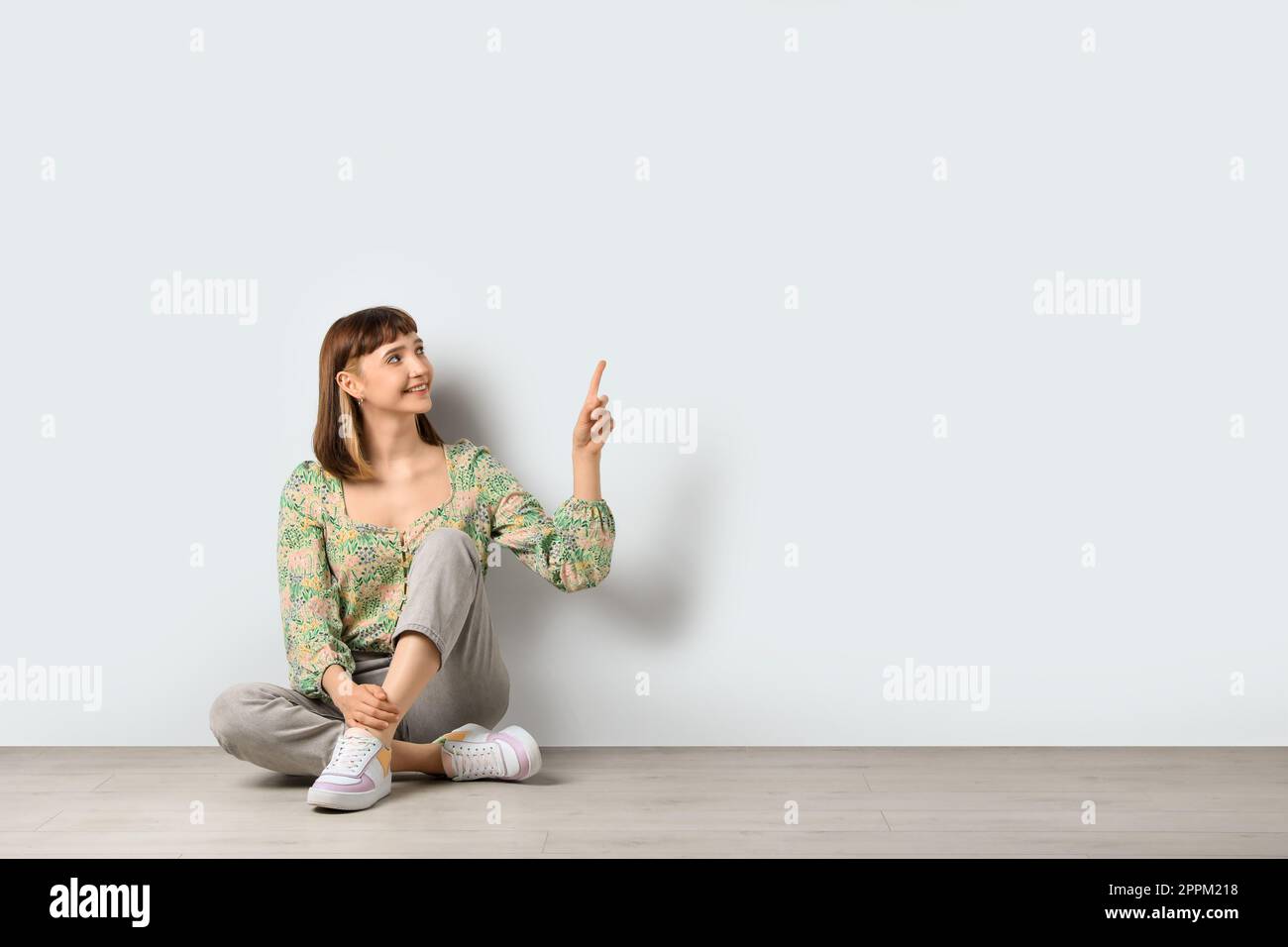 Beautiful young girl sitting on floor and pointing at something against ...