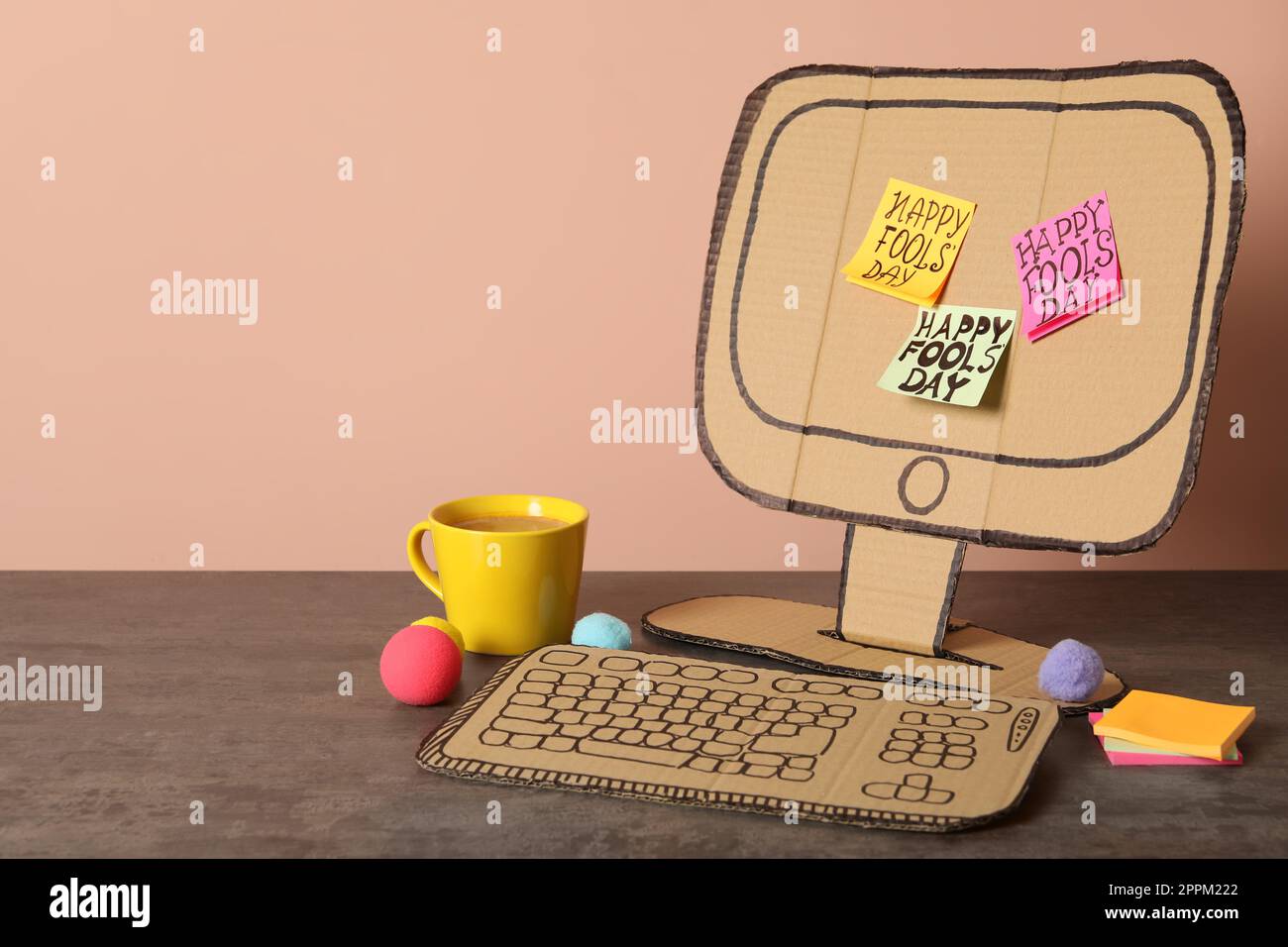 Cardboard computer with Happy Fools' Day notes and cup on wooden table ...