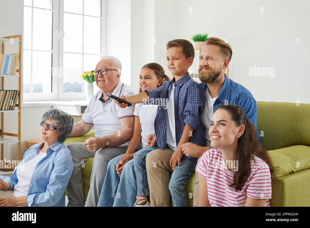 Grandparents, mother, father and two little kids are watching television programs together. Stock Photo