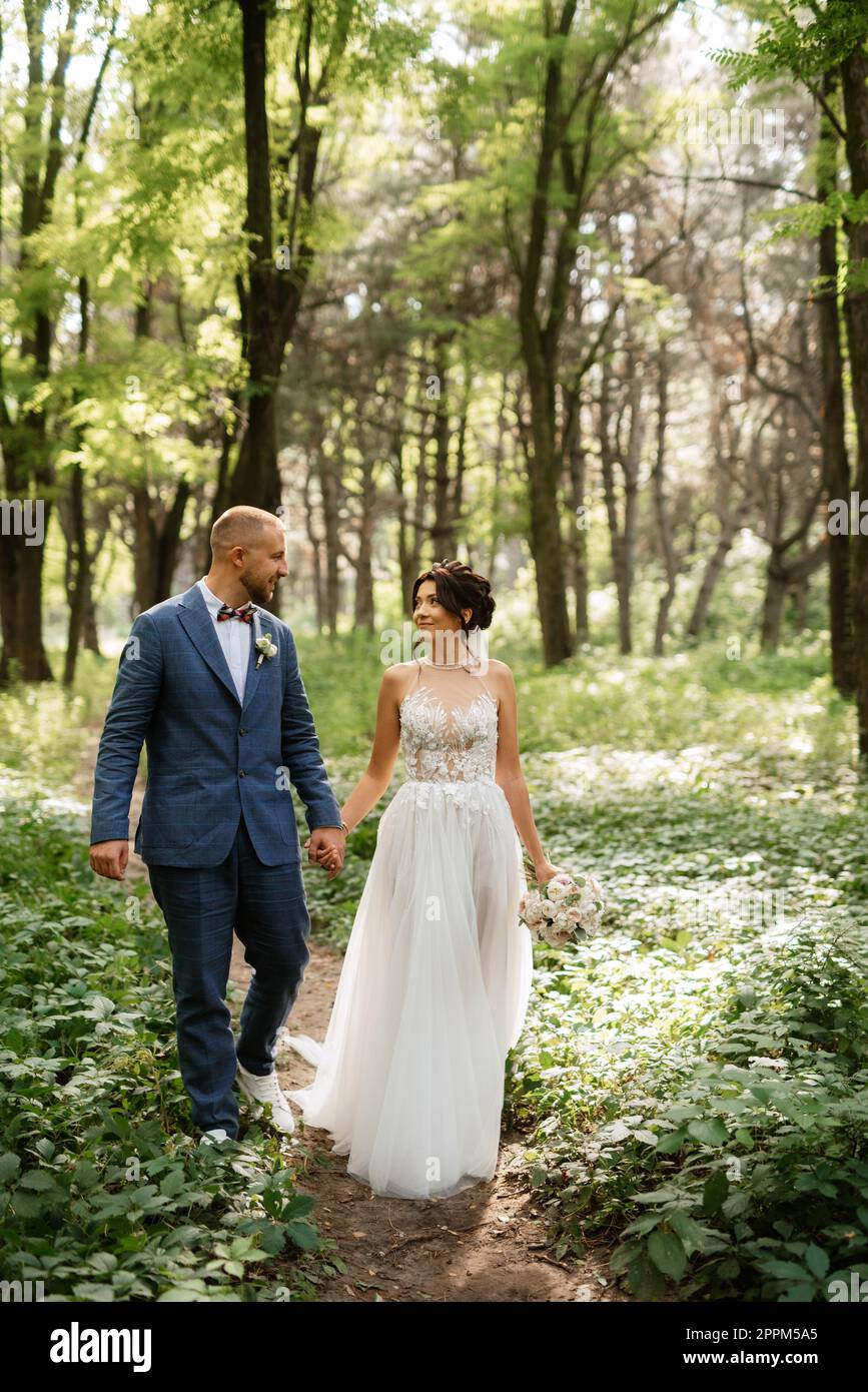 wedding walk of the bride and groom in the deciduous forest in summer ...