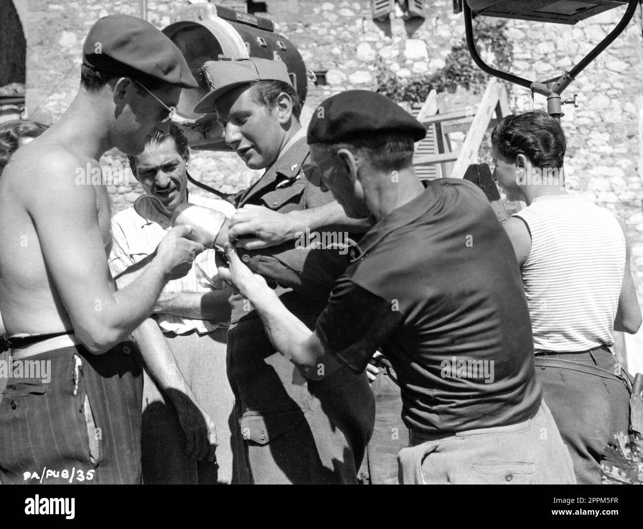 PETER USTINOV in costume as Private Angelo has his artificial arm and hook fixed by Crew Members on set location candid in Central Italy during filming of PRIVATE ANGELO 1949 directors / producers / screenplay MICHAEL ANDERSON and PETER USTINOV novel Eric Linklater costume design Nadia Benois Pilgrim Pictures / Associated British-Pathe Stock Photo