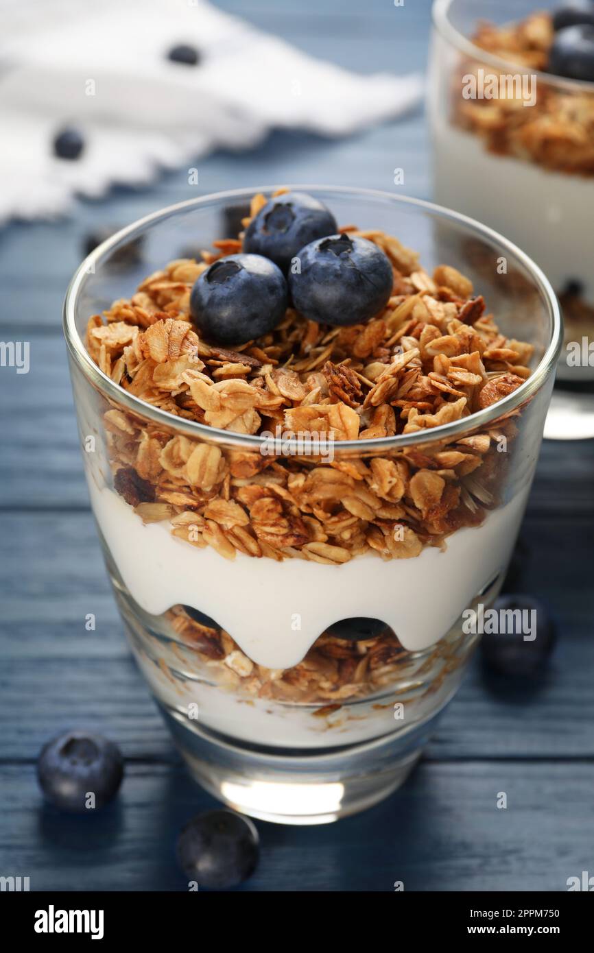 Glass of tasty yogurt with muesli and blueberries on blue wooden table Stock Photo