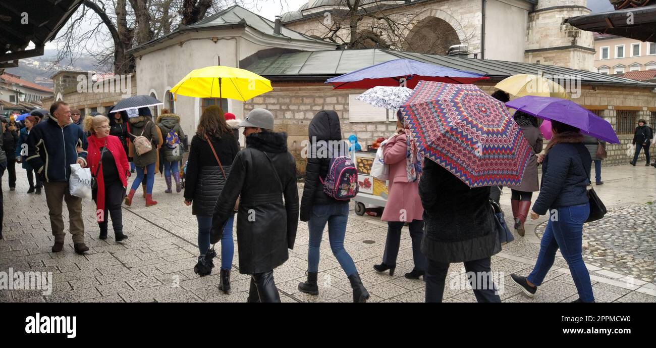 Sarajevo, Bosnia and Herzegovina, March 8, 2020. People on the central streets of Sarajevo. Tourists walk around Bascarsija. Gazi Husrev-begova dzamija mosque. People with umbrellas. Stock Photo