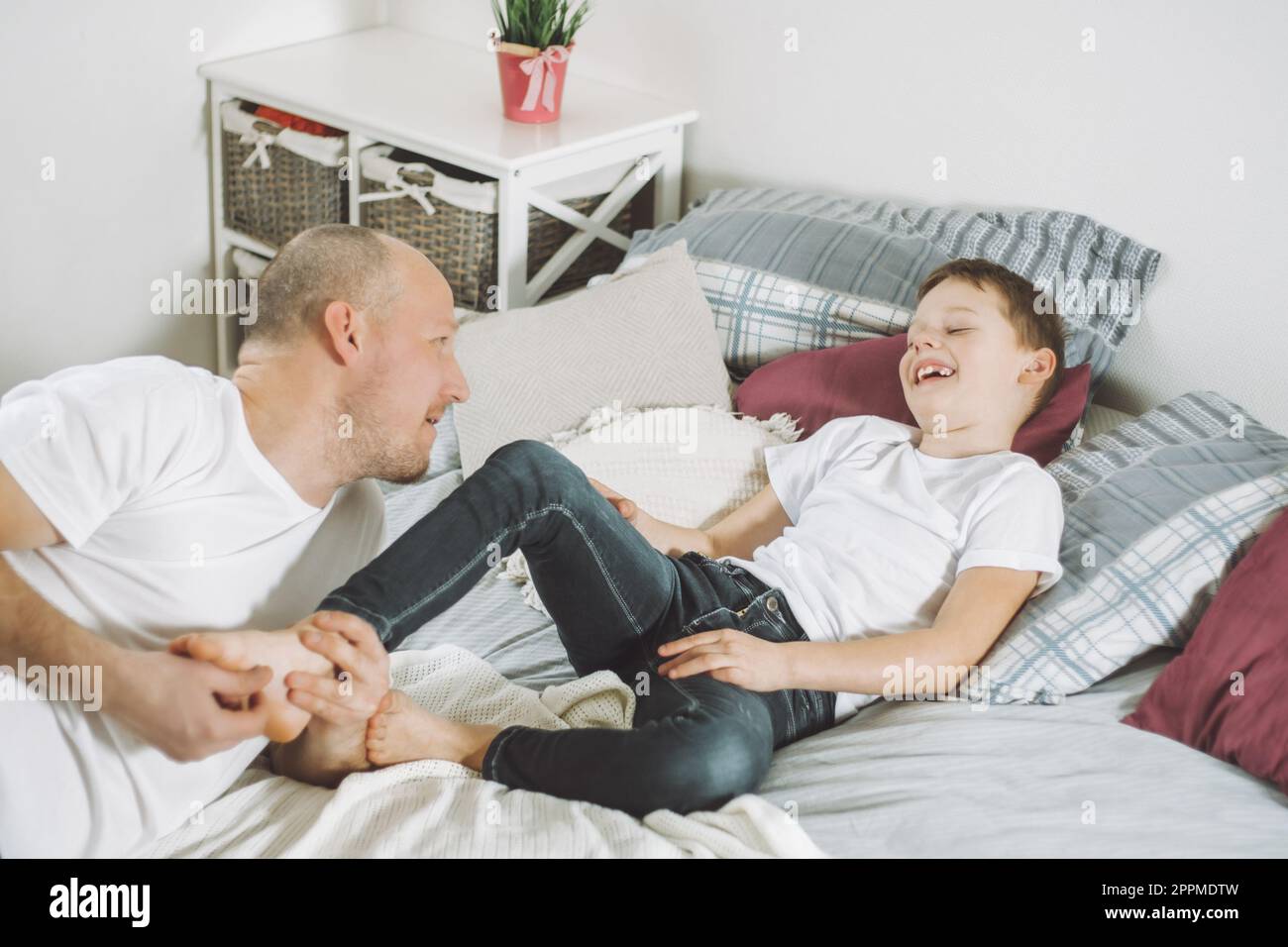 Father plays with his son 7-10 on bed. Dad tickles kids feet. Family, having fun Stock Photo