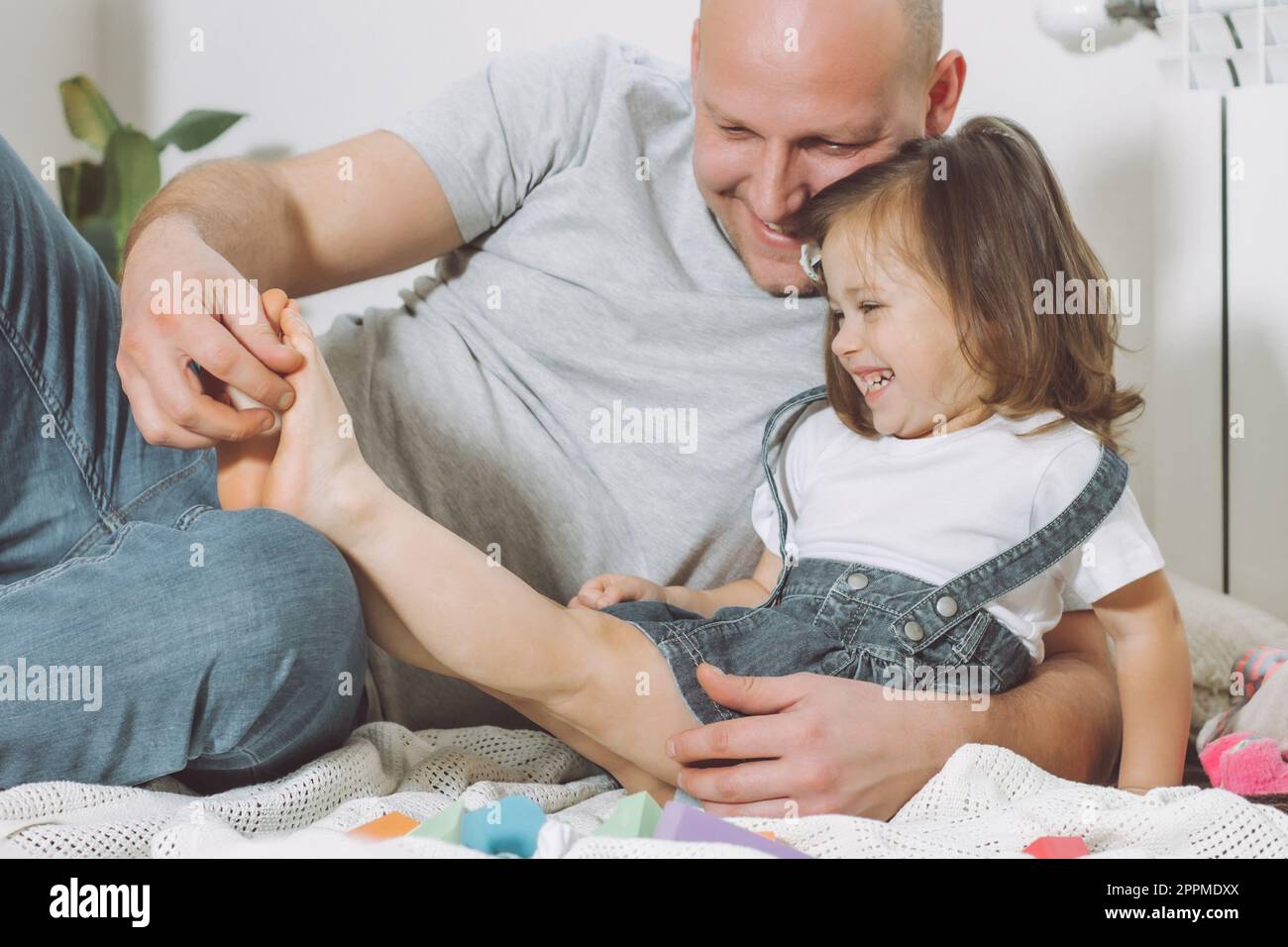 Father plays with little daughter 2-4 on floor. Dad tickles kids feet.  Family having fun Stock Photo - Alamy