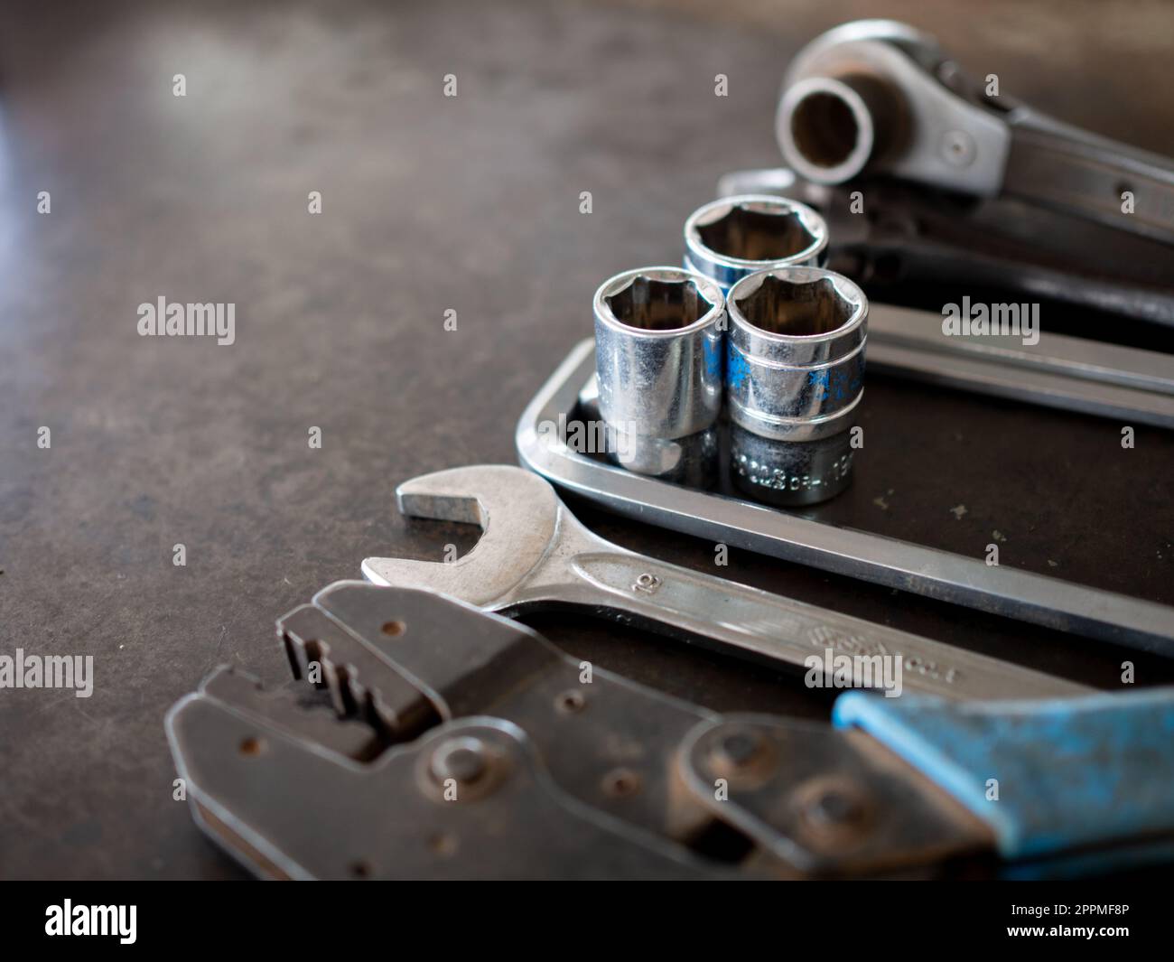 Hand tools consisting of wrenches, pliers, socket wrenches, laid out on old steel plate background. Stock Photo