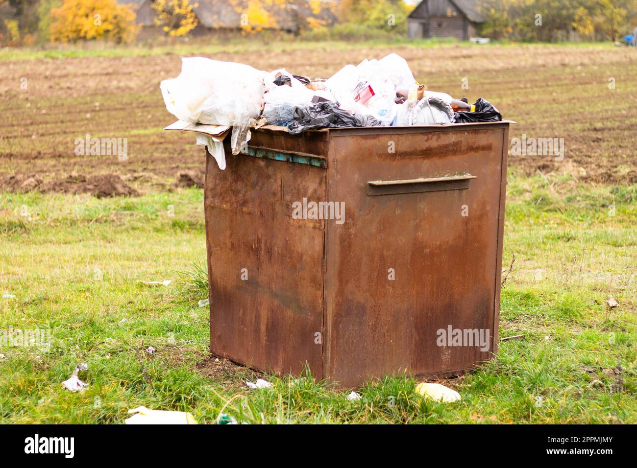 Overflowing rusty trash can in the countryside. Rubbish scattered on the ground, environmental protection problem Stock Photo