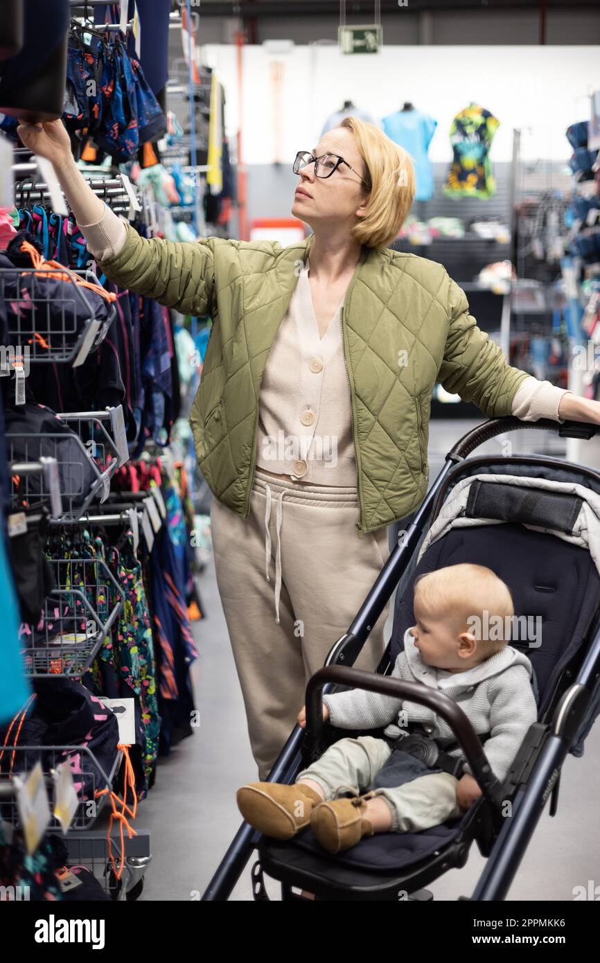 Casualy dressed mother choosing sporty shoes and clothes products in