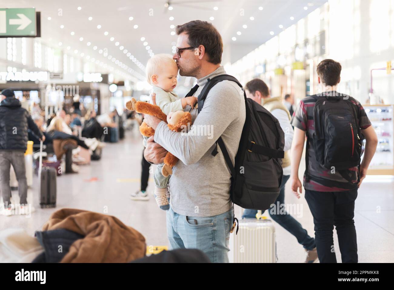 Father traveling with child, holding and kising his infant baby boy at airport terminal waiting to board a plane. Travel with kids concept. Stock Photo