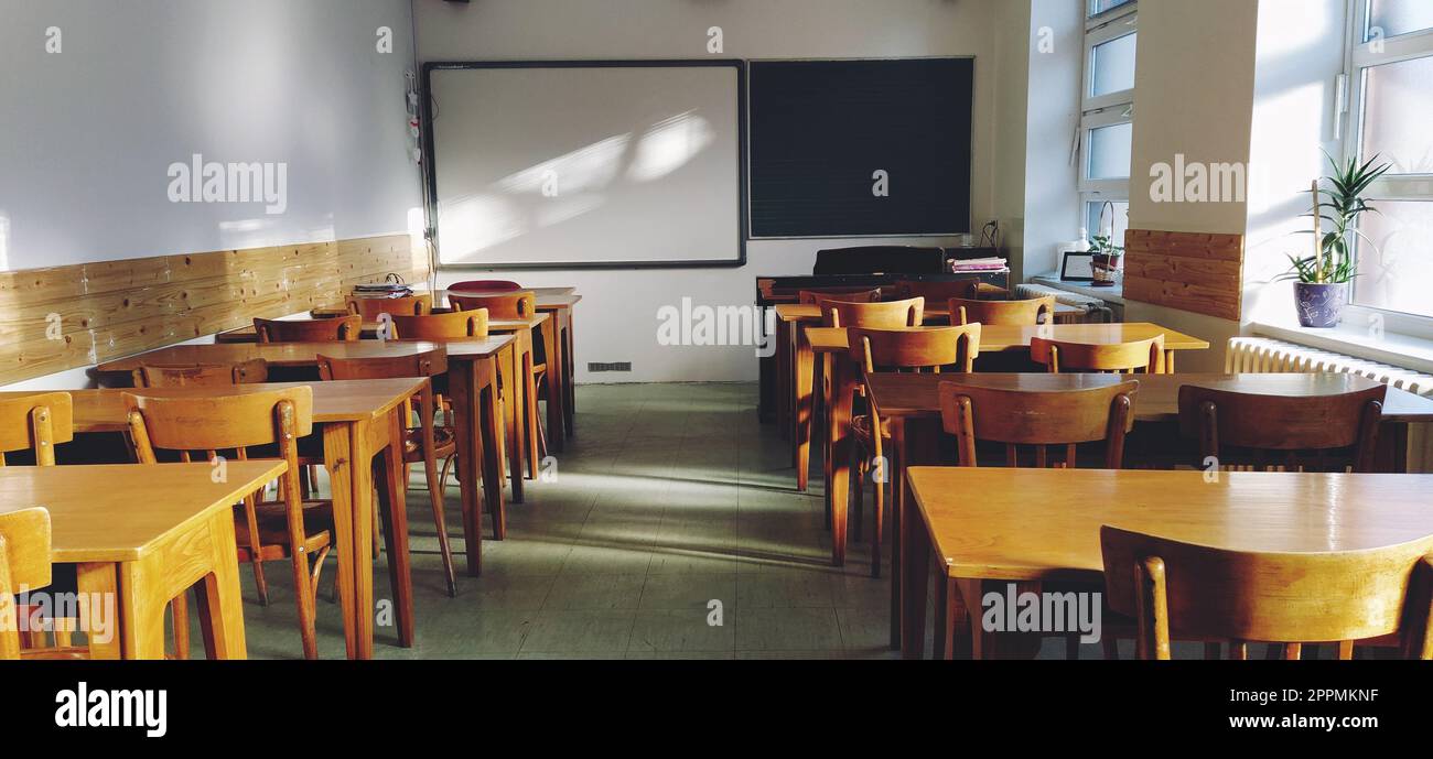 Music solfeggio empty class at school. The sun's rays fall on the floor through the window. Wooden student tables and chairs. School board and white walls. School interior. Stock Photo