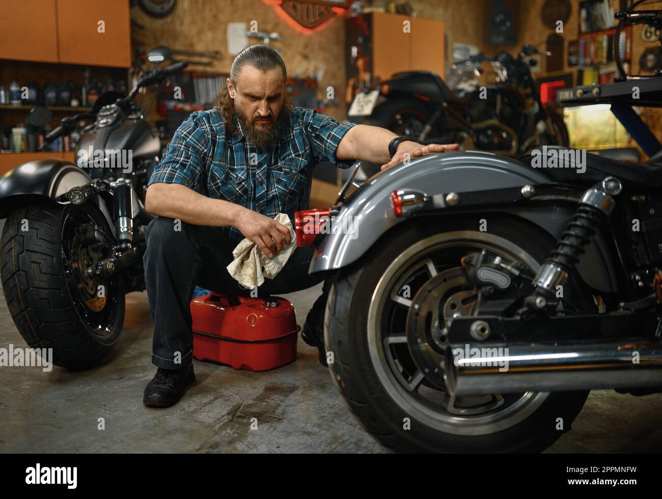 Bearded mature man biker cleaning motorcycle in garage workstation Stock Photo