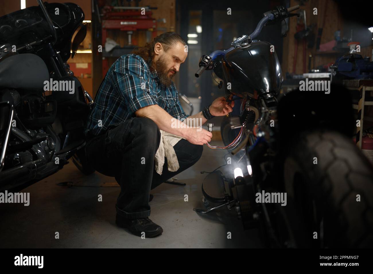 Mature man biker repairing motorcycle in garage at evening Stock Photo