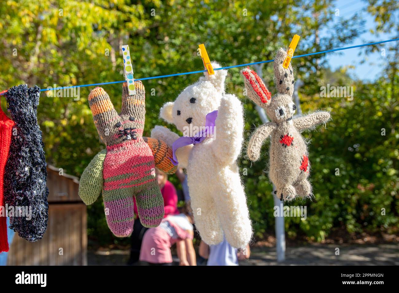 Childrens soft toys. Handmade white teddy bear and plush bunnies on clothesline over blurred natural background. Fixed with clothespins. Stock Photo