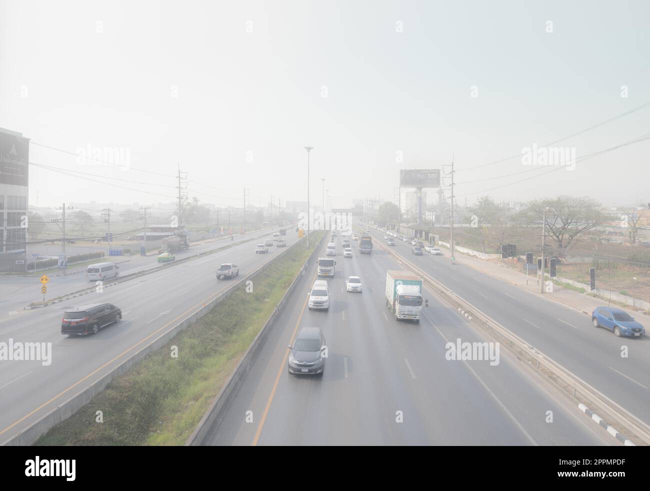 PATHUM THANI, THAILAND-MARCH 10, 2023: Cars driving on highway road with air pollution. Smog and fine dust of pm2.5 covered city. Polluted air. Dirty environment. Urban toxic dust. Unhealthy air. Stock Photo