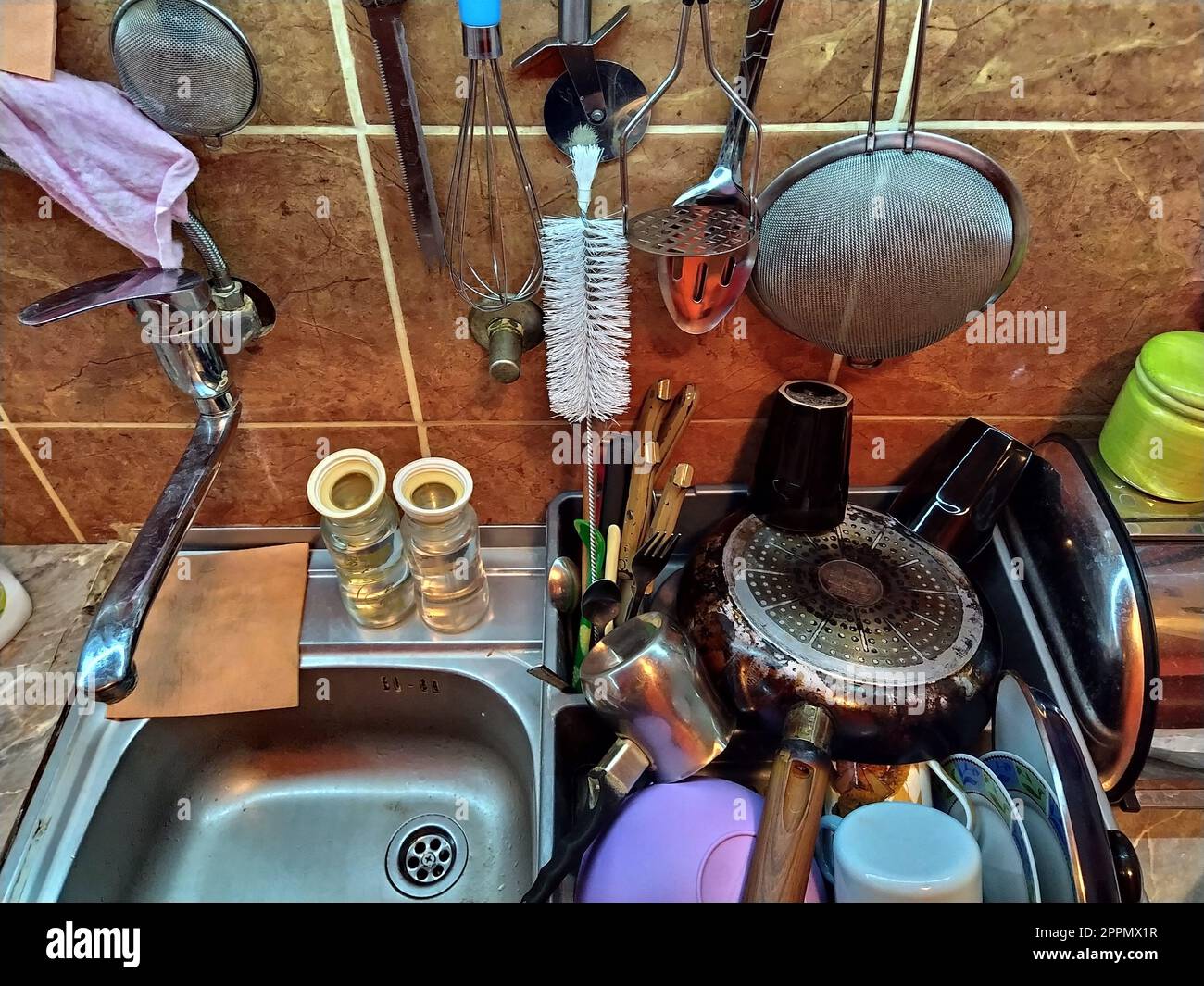 Belgrade, Serbia, December 12, 2020. Kitchen, countertop with sink, top view. Home daily life. The washed dishes are stacked near the sink. Kitchenware is hung on the tile wall. Colander, sponges rags Stock Photo